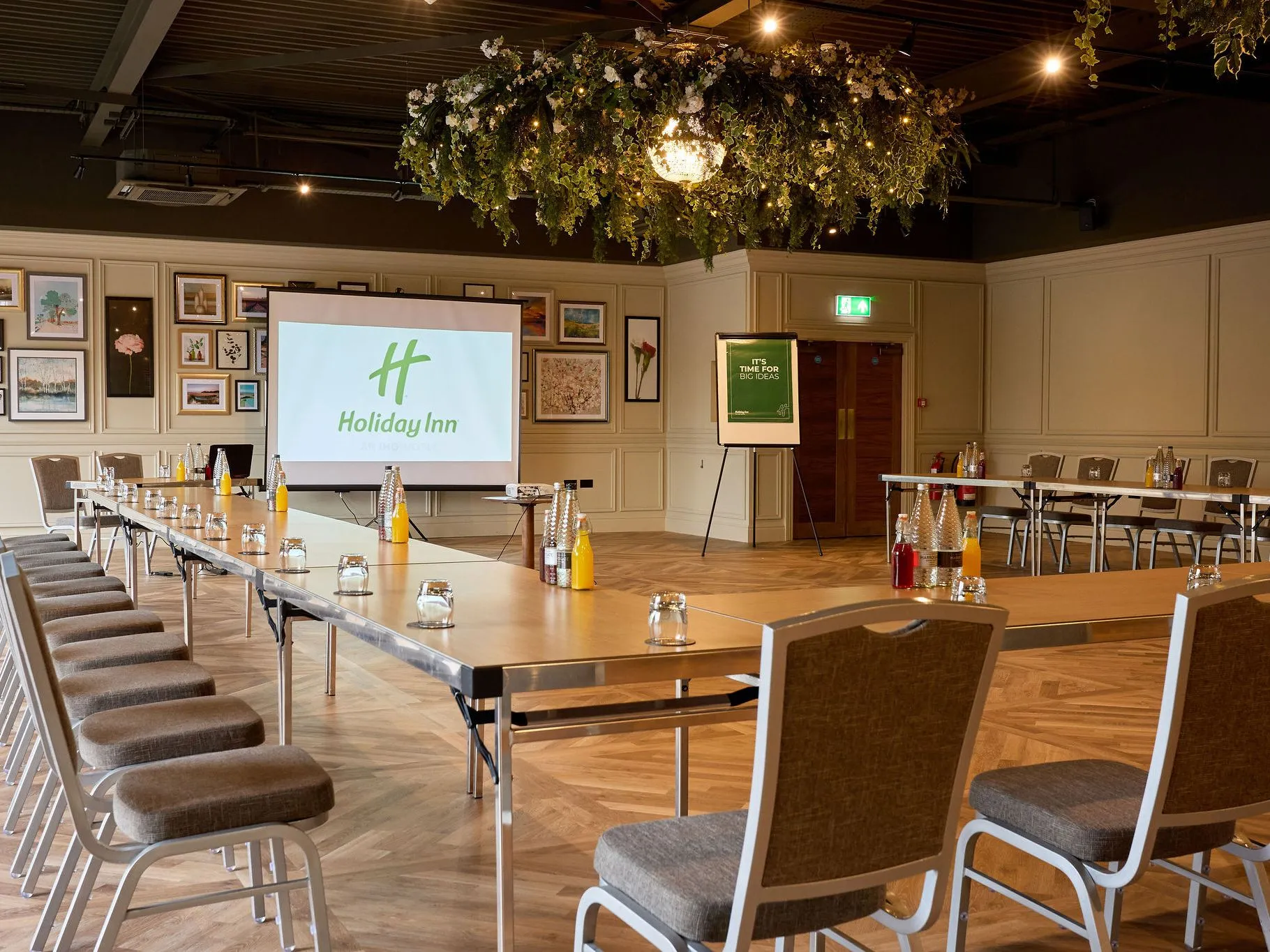 Meeting room set up in a U-shape with tables, chairs, bottled drinks and a presentation screen at Holiday Inn.