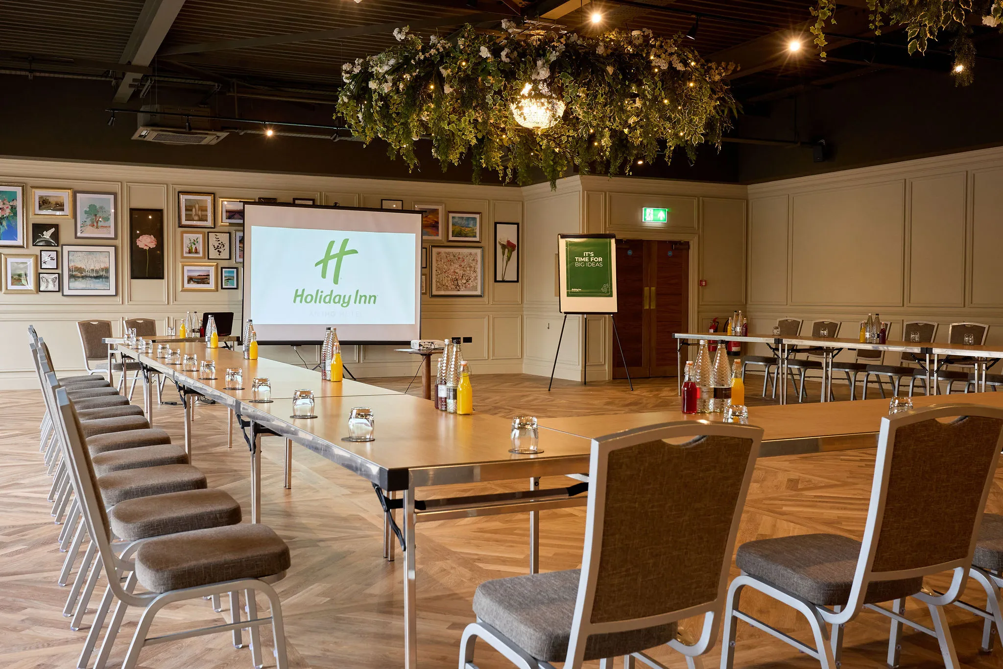 Meeting room set up in a U-shape with tables, chairs, bottled drinks and a presentation screen at Holiday Inn.