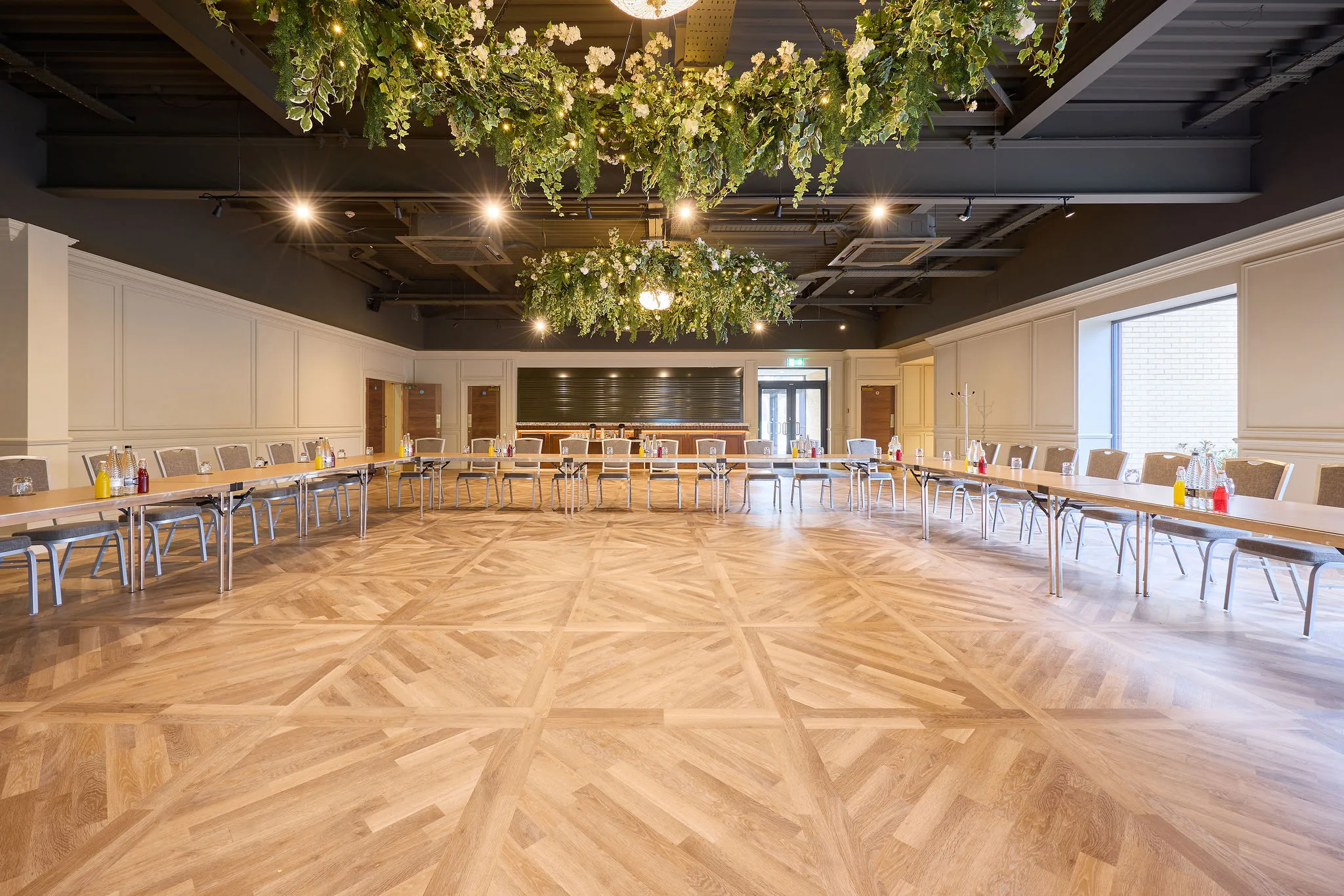 Spacious event room with U-shaped tables, floral ceiling installations and parquet flooring