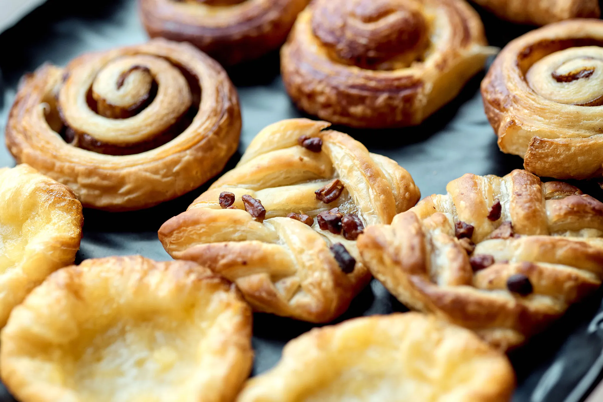 Assorted freshly baked pastries including cinnamon swirls and flaky pastries with chocolate pieces on a tray