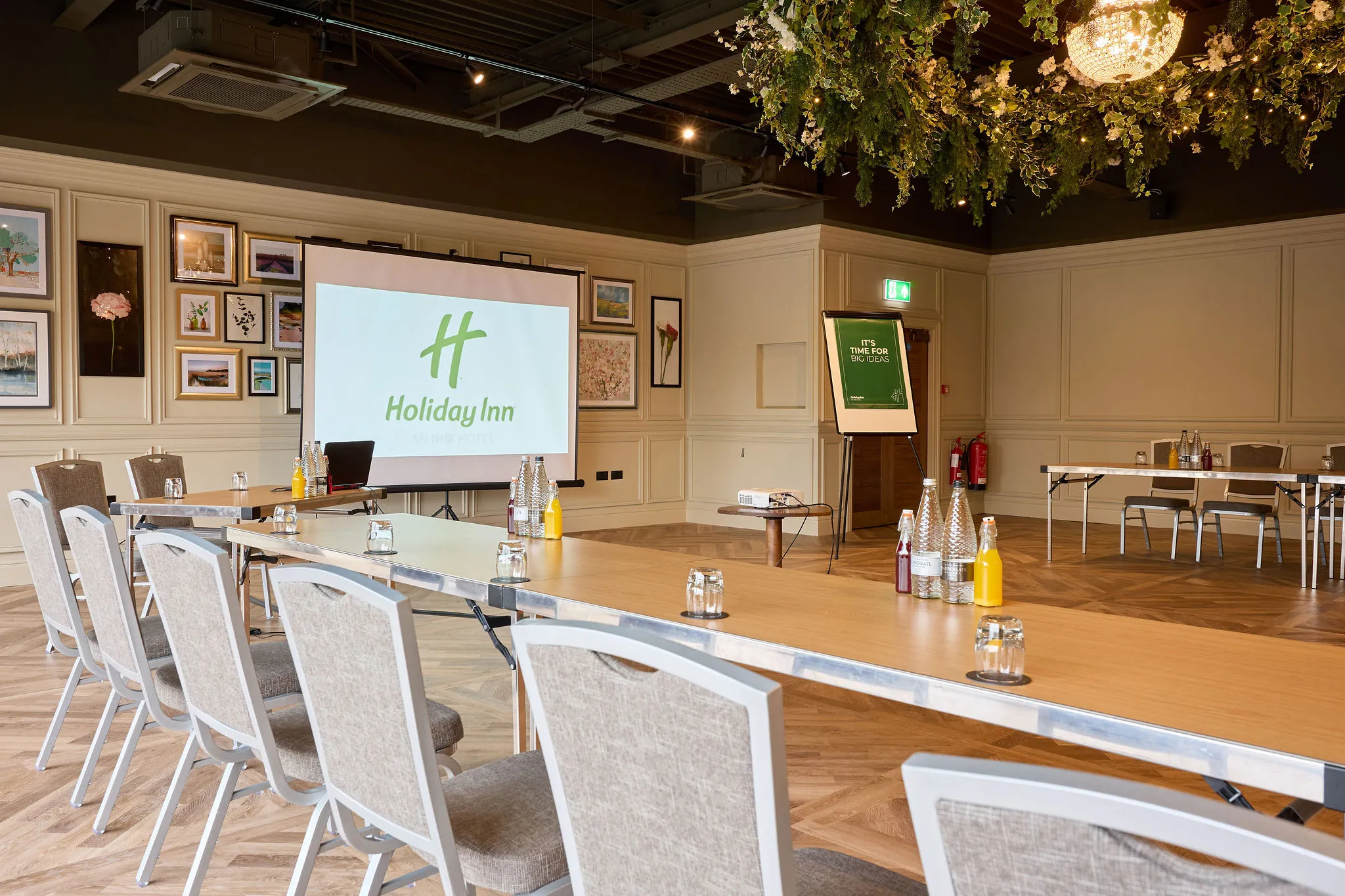 Meeting room at Holiday Inn set up with tables, chairs, projector screen and refreshments