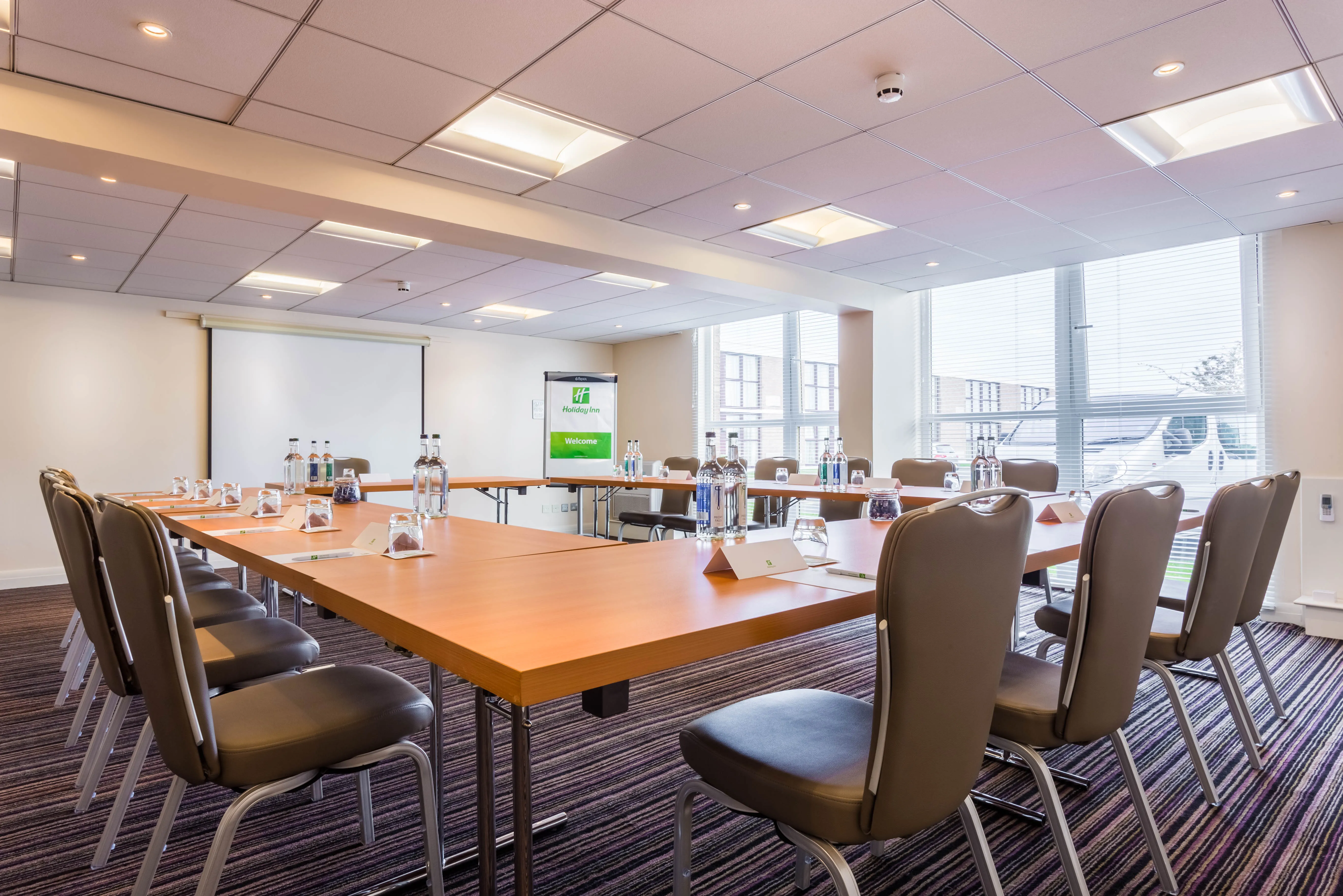 Vickers meeting room set up in a boardroom layout with tables, chairs, bottled water and a presentation screen
