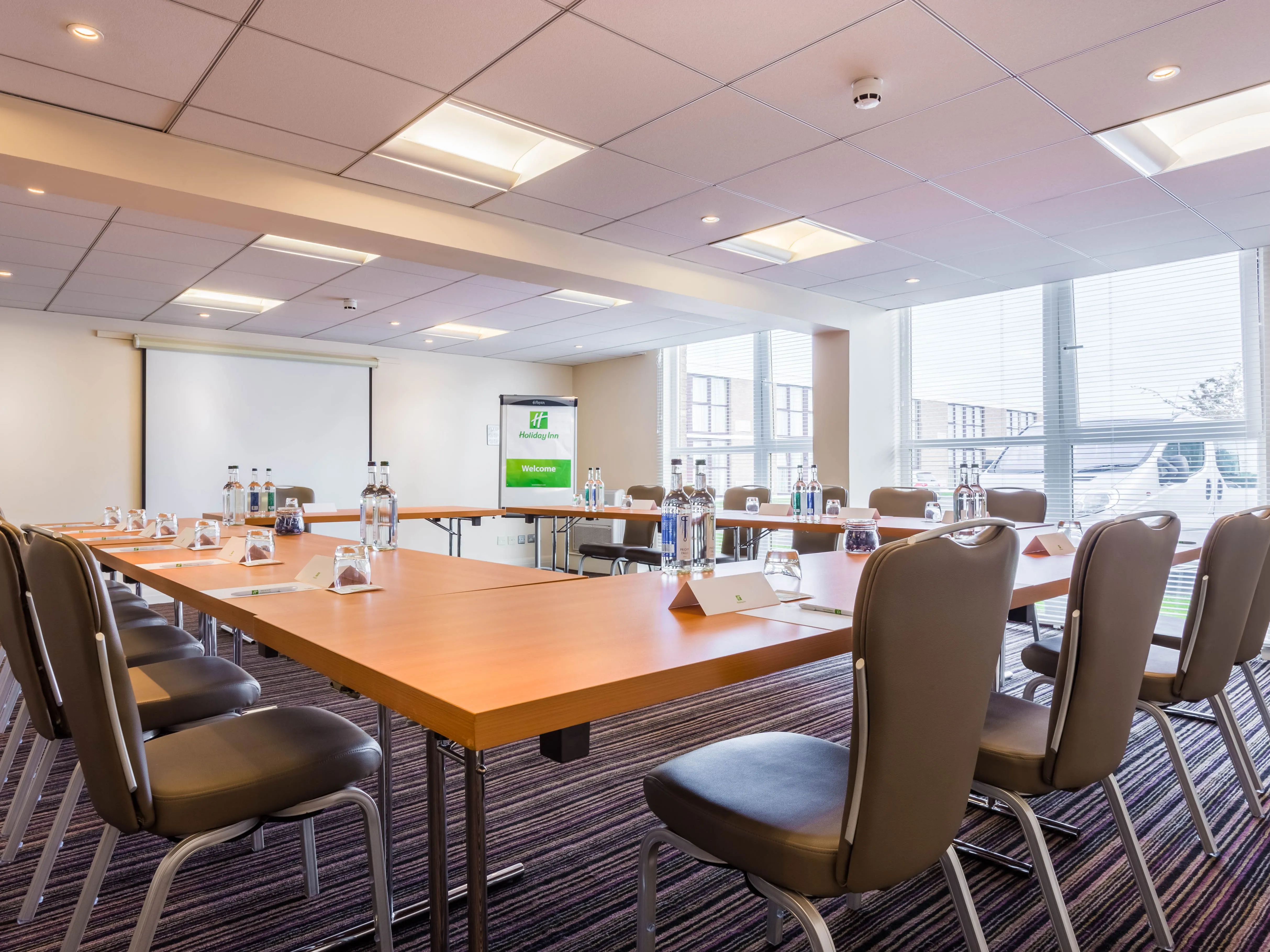 Vickers meeting room set up in a boardroom layout with tables, chairs, bottled water and a presentation screen