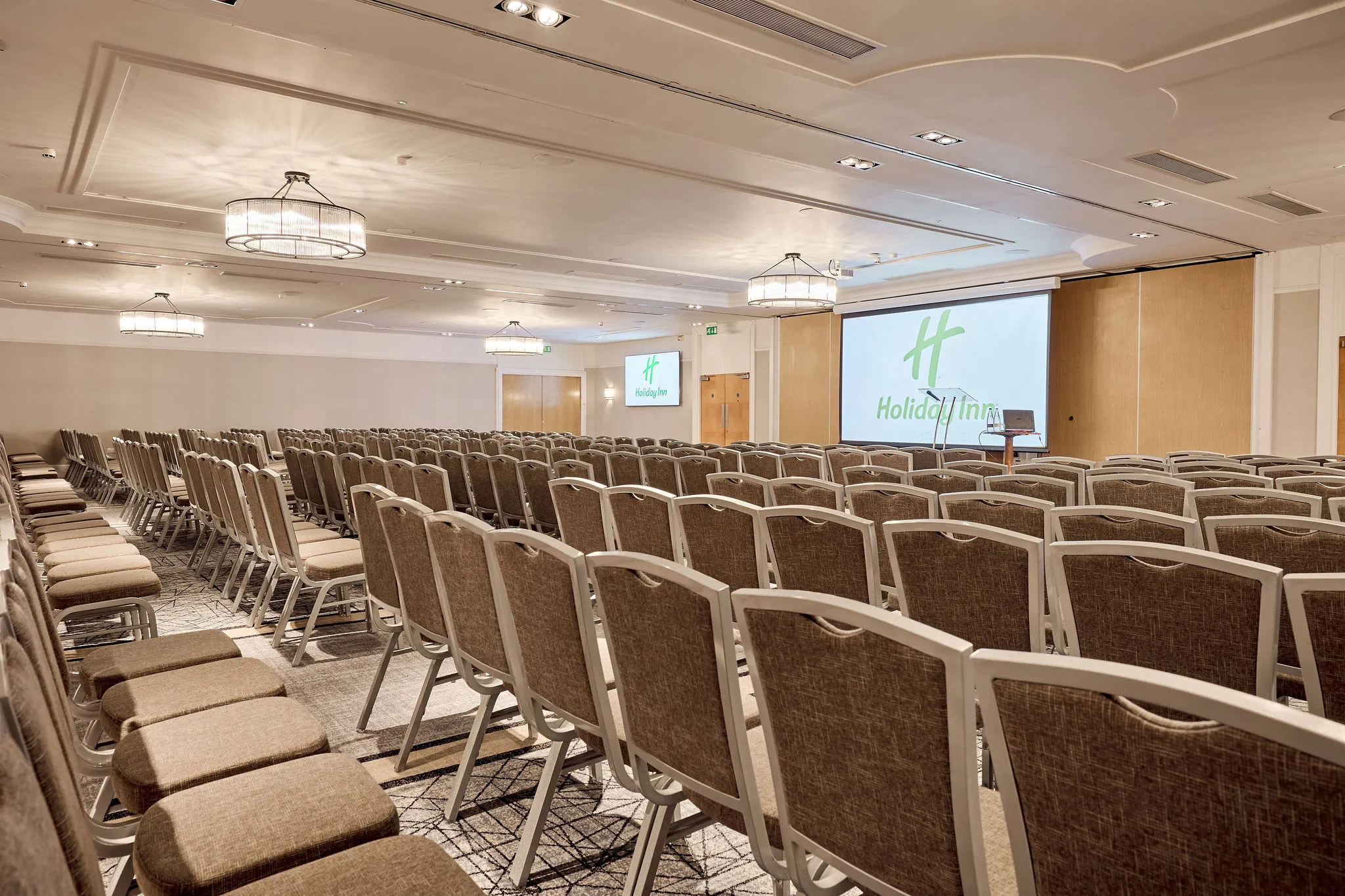 Conference room with rows of chairs facing a presentation screen and lectern at Holiday Inn