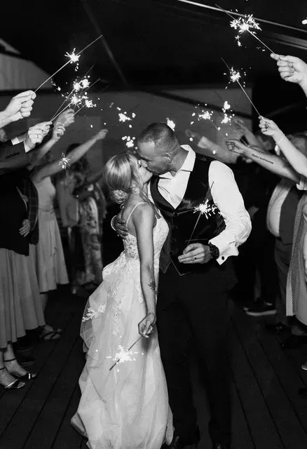 Newlyweds kissing beneath a tunnel of sparklers held by wedding guests.