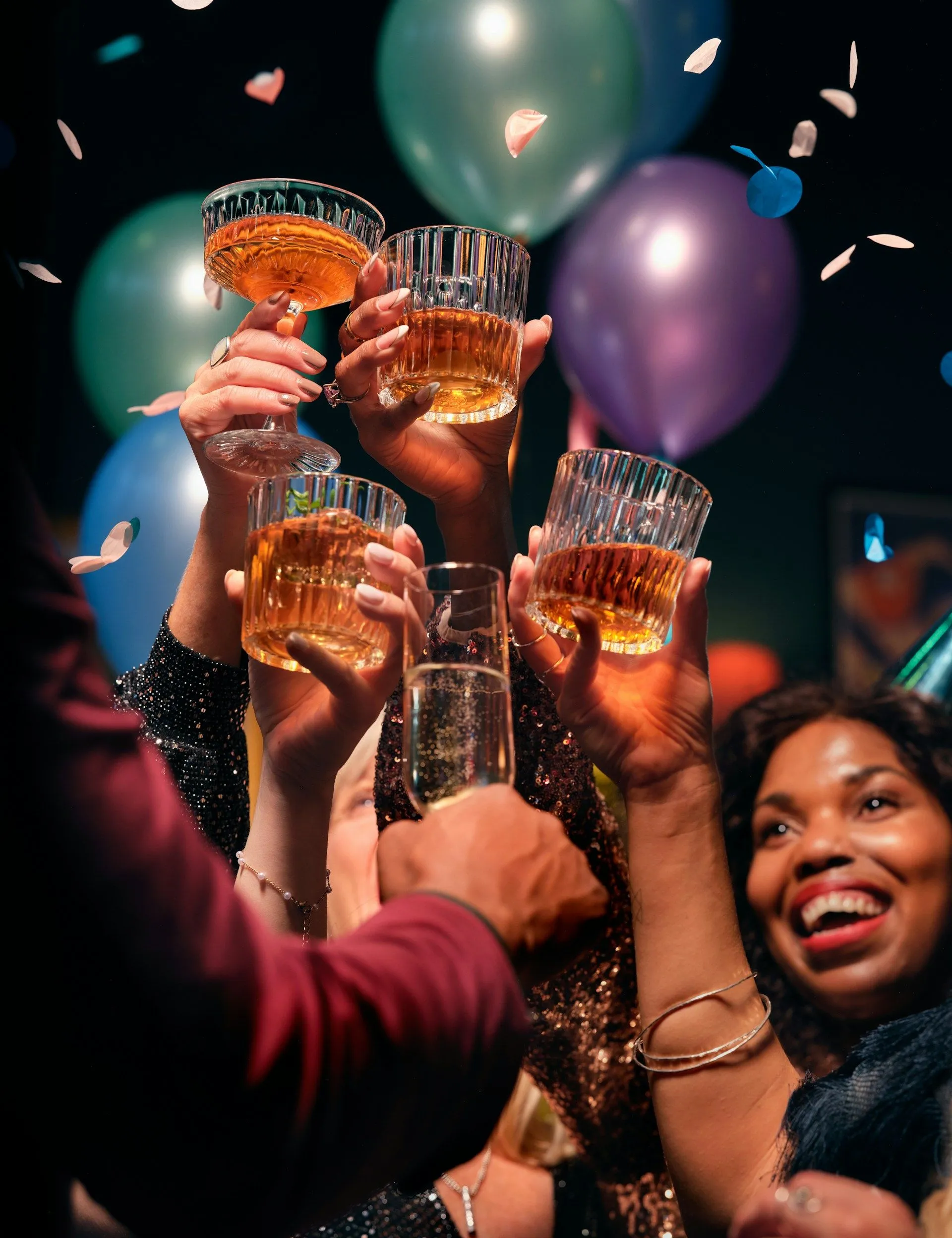 Friends raising glasses in a festive toast with balloons and confetti in the background