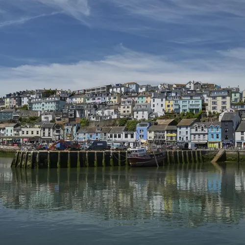 Colourful hillside houses overlooking a harbour with calm water reflections under a blue sky