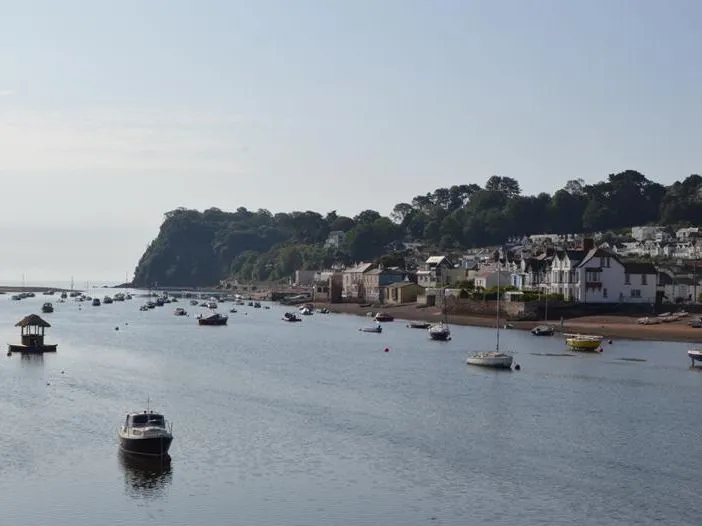 Boats moored on the calm harbour at Shaldon with a row of seaside houses along the shoreline