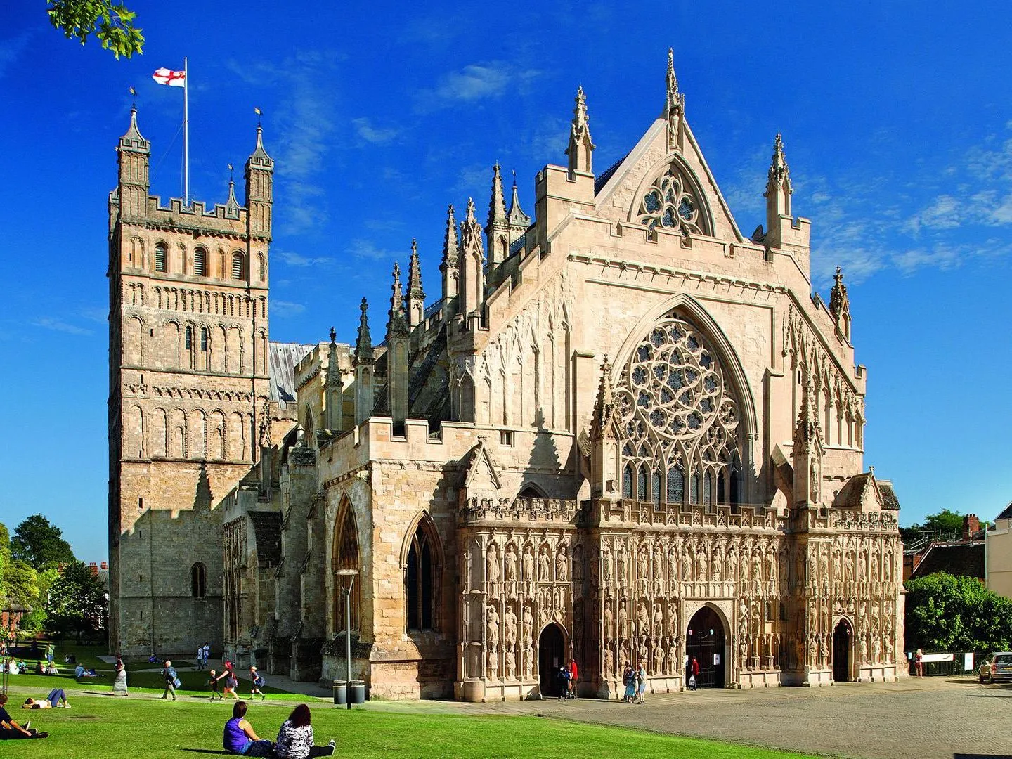 Exeter Cathedral in Devon, England, with people on the green under a bright blue sky