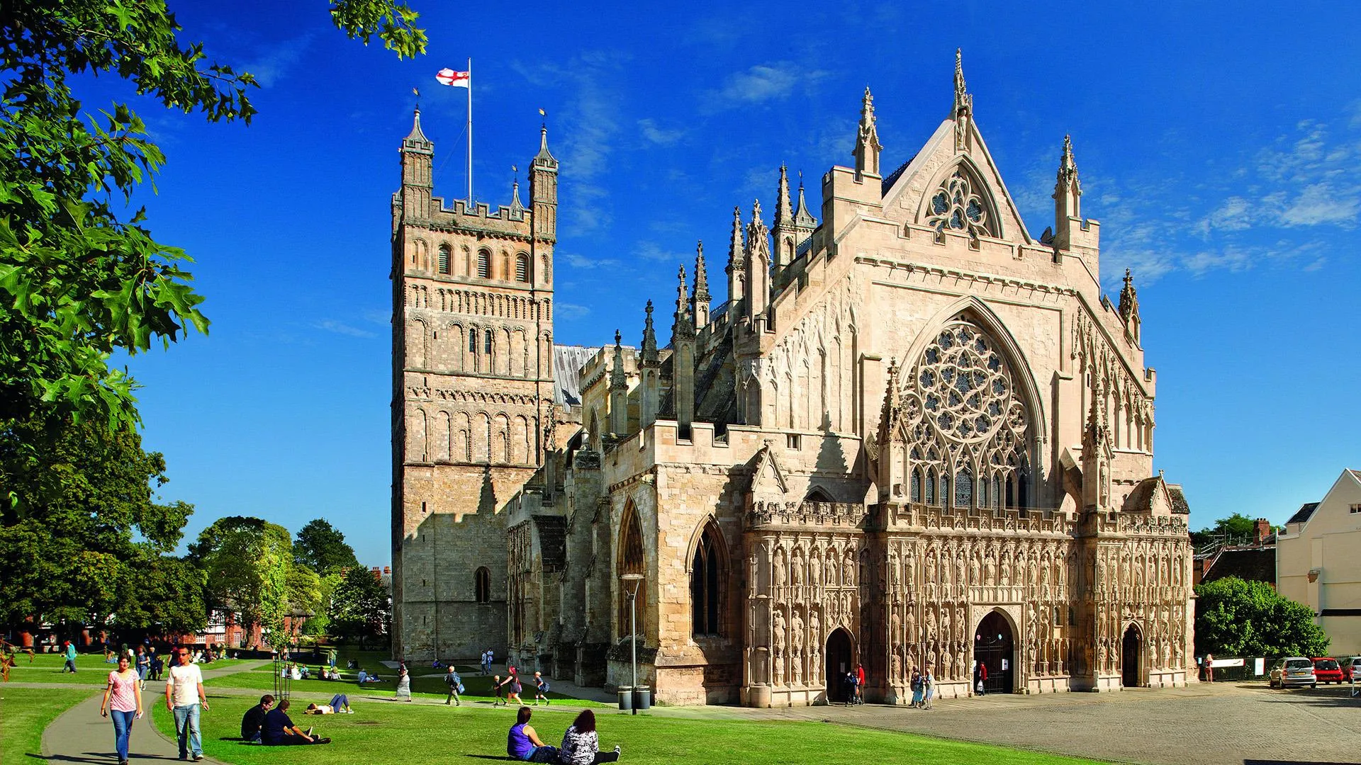 Exeter Cathedral in Devon, England, with people on the green under a bright blue sky