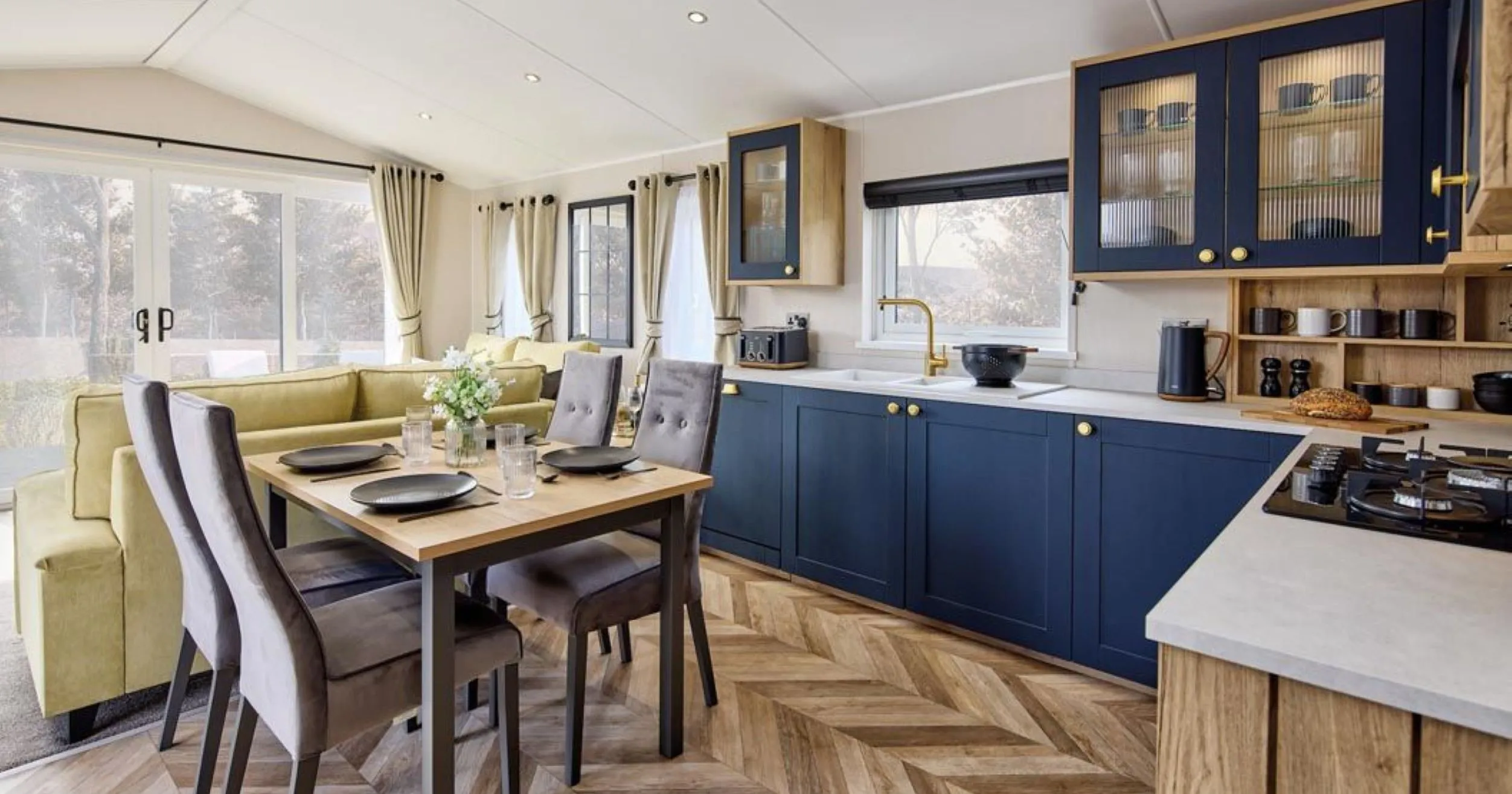 Modern open-plan kitchen and dining area with navy cabinets, wooden table and grey chairs