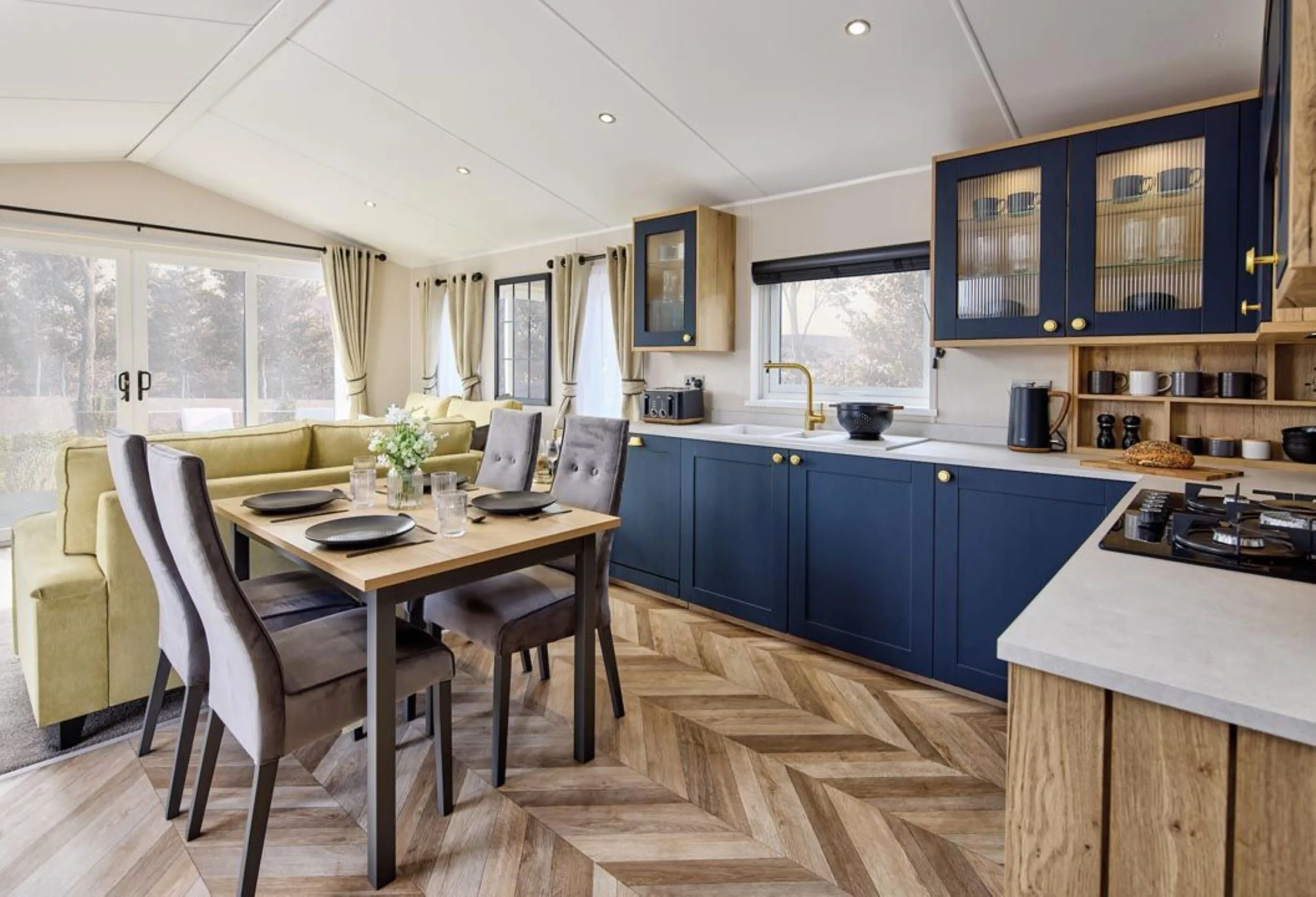 Modern open-plan kitchen and dining area with navy cabinets, wooden table and grey chairs