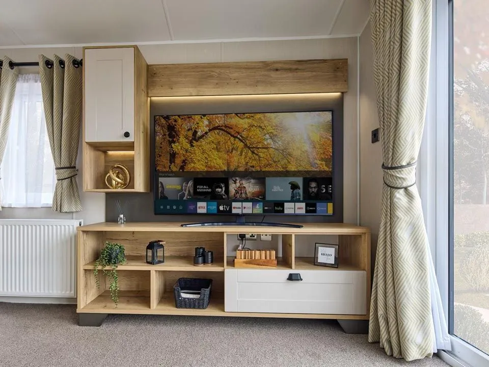 Modern living room TV unit with wood and cream cabinetry, shelves and patterned curtains