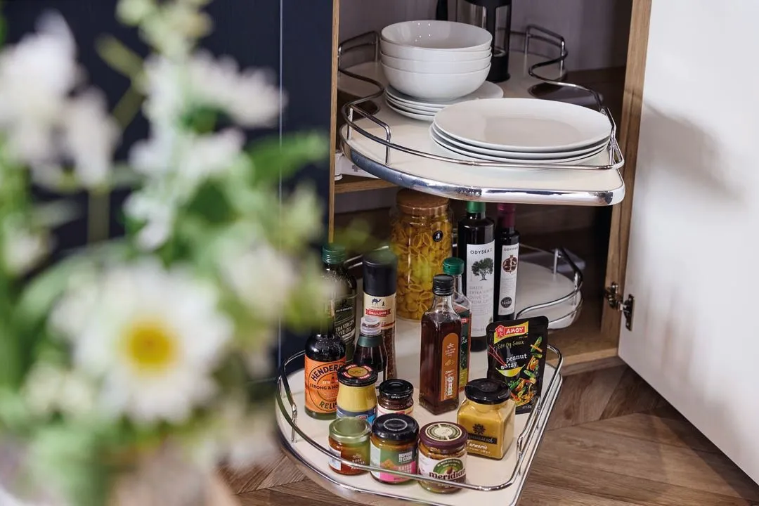 Corner kitchen cupboard with pull-out shelves holding plates, bowls, bottles and jars