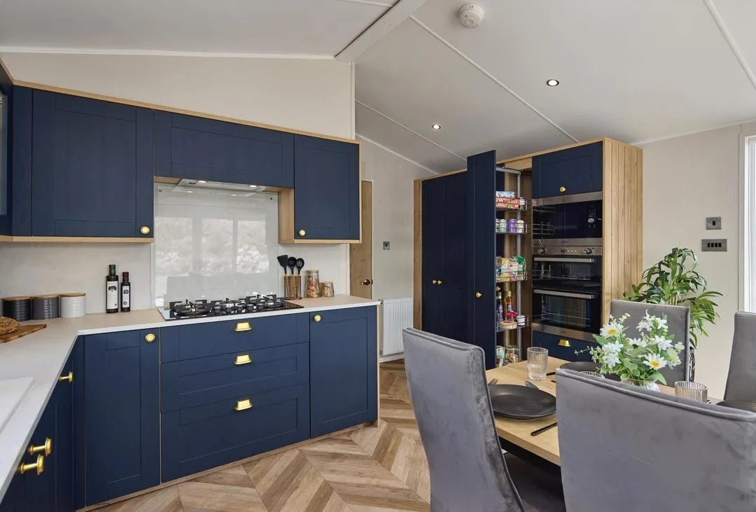 Modern kitchen with navy blue cabinets, brass handles and built-in ovens beside a dining table