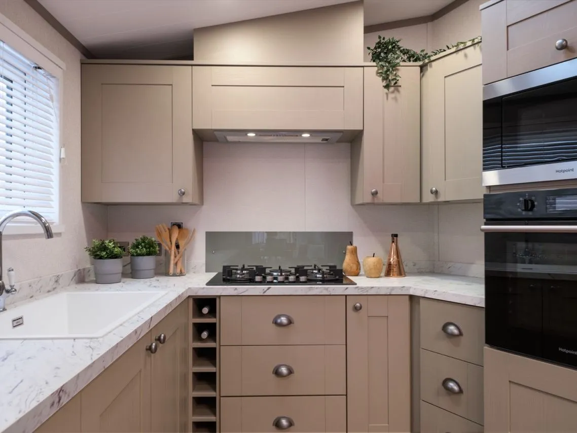 Modern L-shaped kitchen with beige cabinets, marble-effect worktop, gas hob and built-in double oven