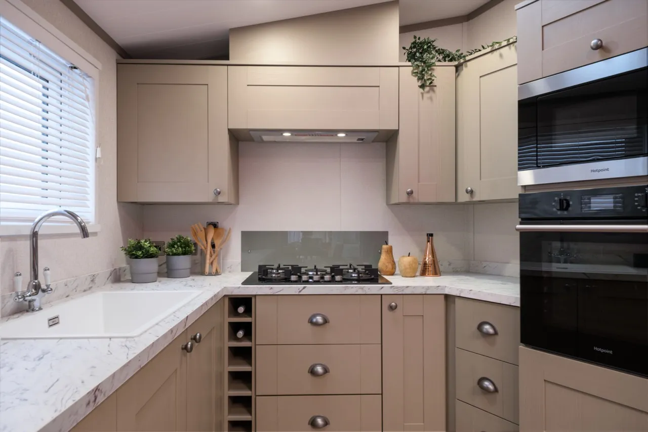 Modern L-shaped kitchen with beige cabinets, marble-effect worktop, gas hob and built-in double oven