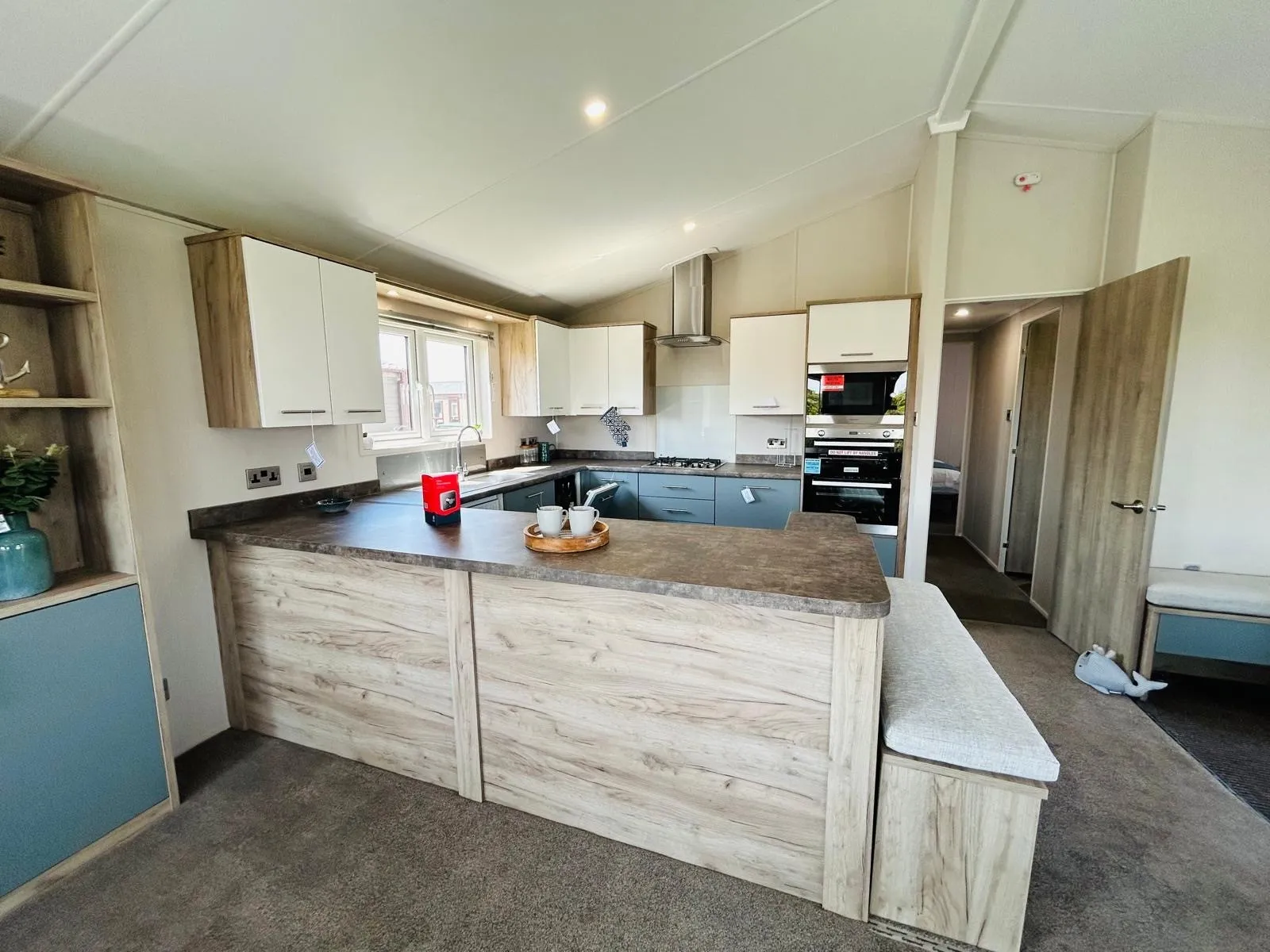 Modern open-plan kitchen with breakfast bar, white and wood-effect cabinets, and built-in oven
