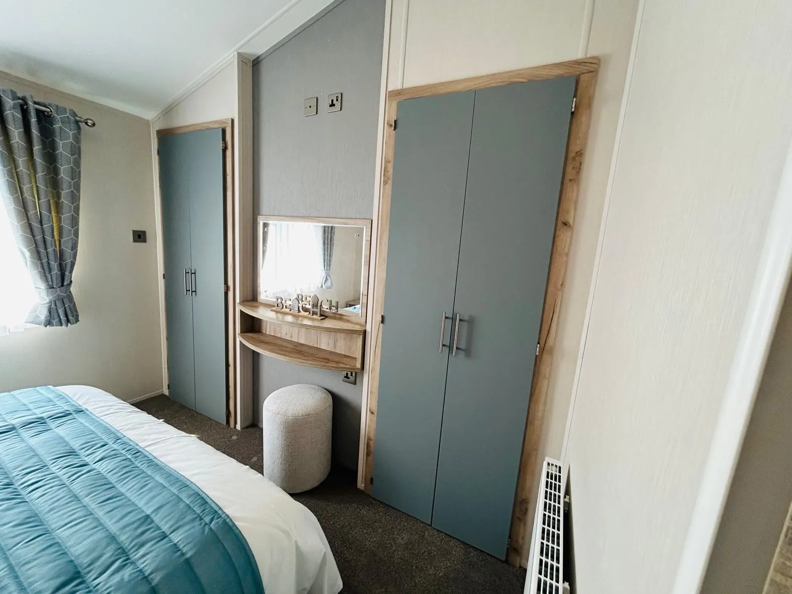 Modern bedroom with blue wardrobe doors, bedside shelves and mirror, and a bed with a teal quilt.