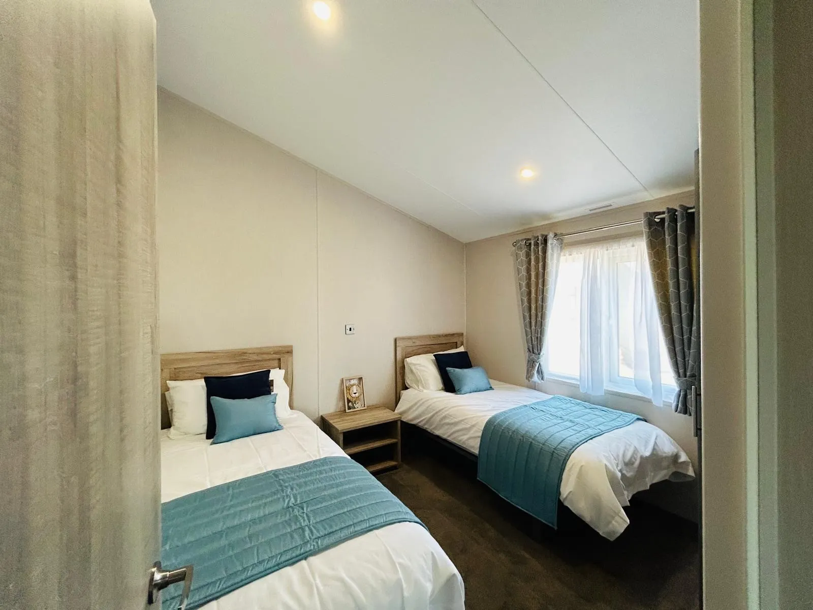 Small twin bedroom with two single beds, blue throws and cushions, and a window with grey curtains