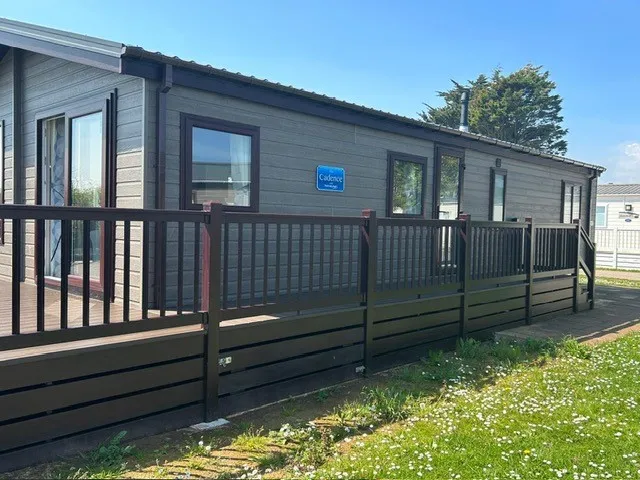 Modern grey static caravan with wooden decking and railing on a sunny day