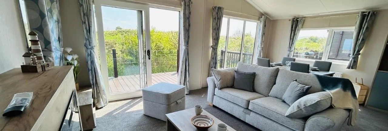 Modern living room with grey sofa, coffee table and large patio doors opening onto a deck