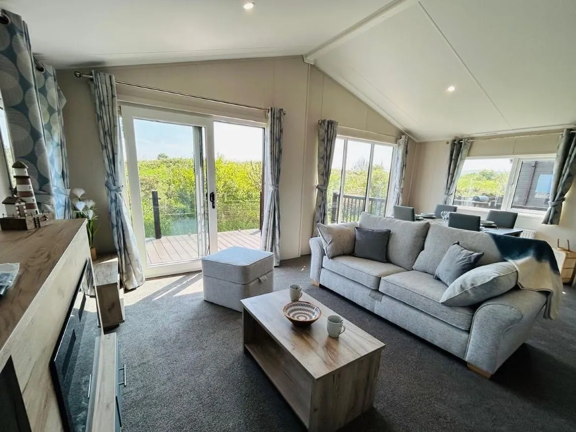 Modern living room with grey sofa, coffee table and large patio doors opening onto a deck