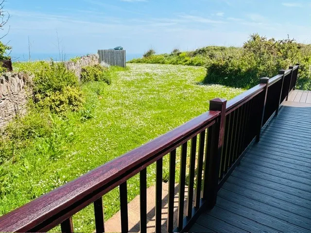 Wooden deck with railing overlooking a grassy coastal garden and the sea