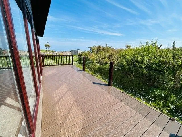 Wooden decked terrace beside a glass-fronted building, overlooking coastal greenery and blue sky