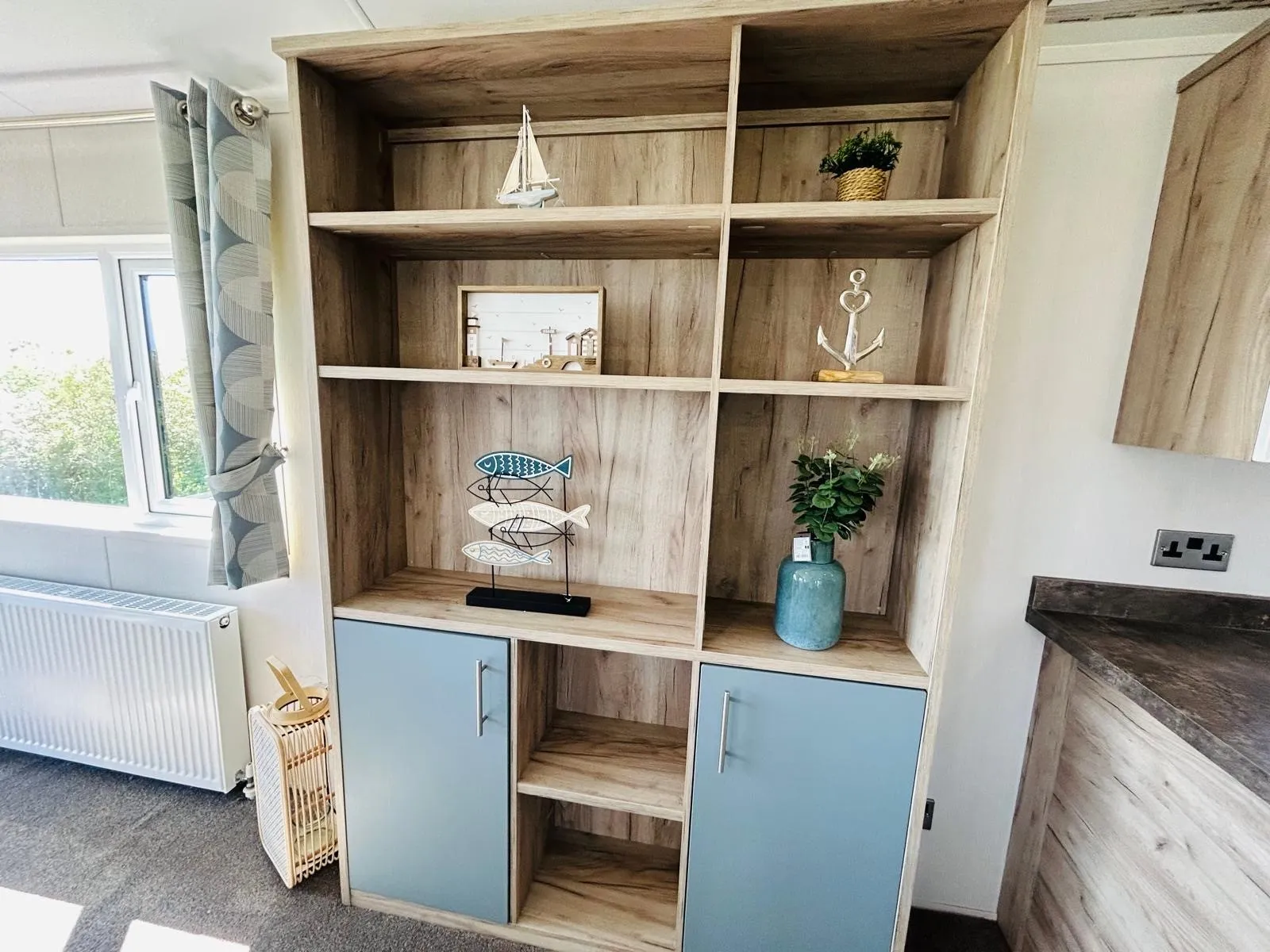 Wooden shelving unit with blue cupboard doors and nautical ornaments in a bright room
