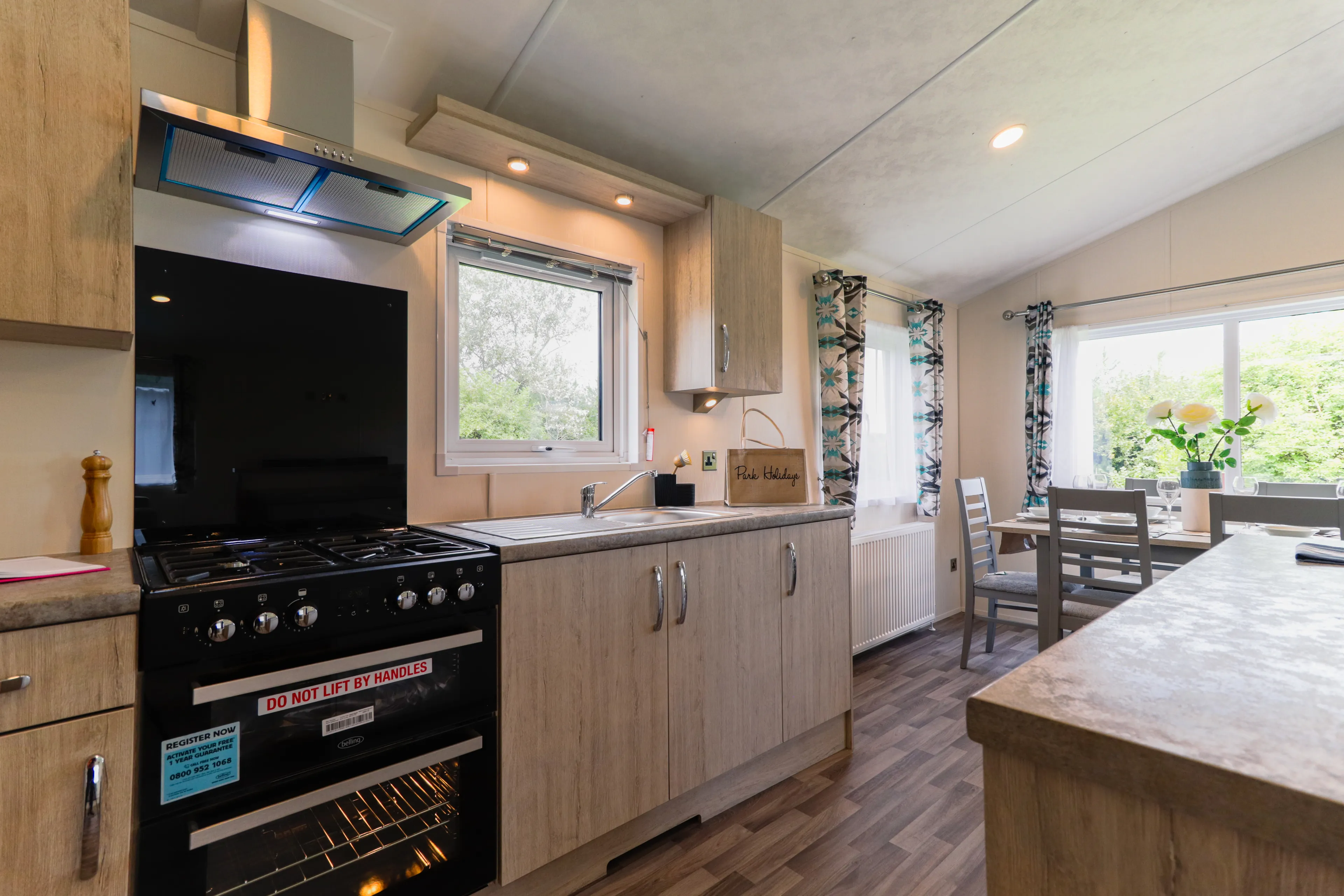Modern kitchen with black cooker, wooden cabinets, sink and a small dining table by a bright window