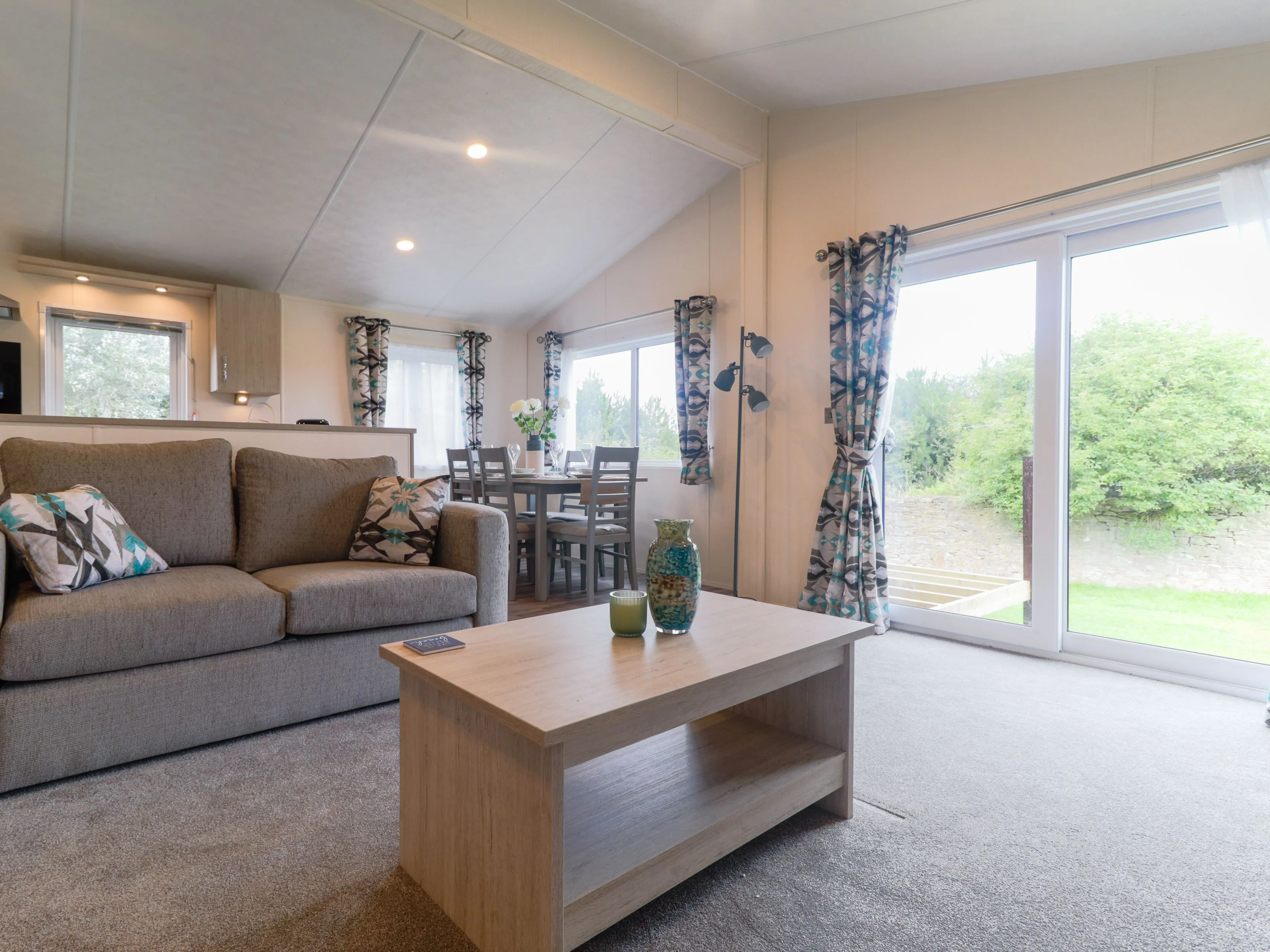 Modern open-plan living area with grey sofa, wooden coffee table, dining table and large sliding glass doors