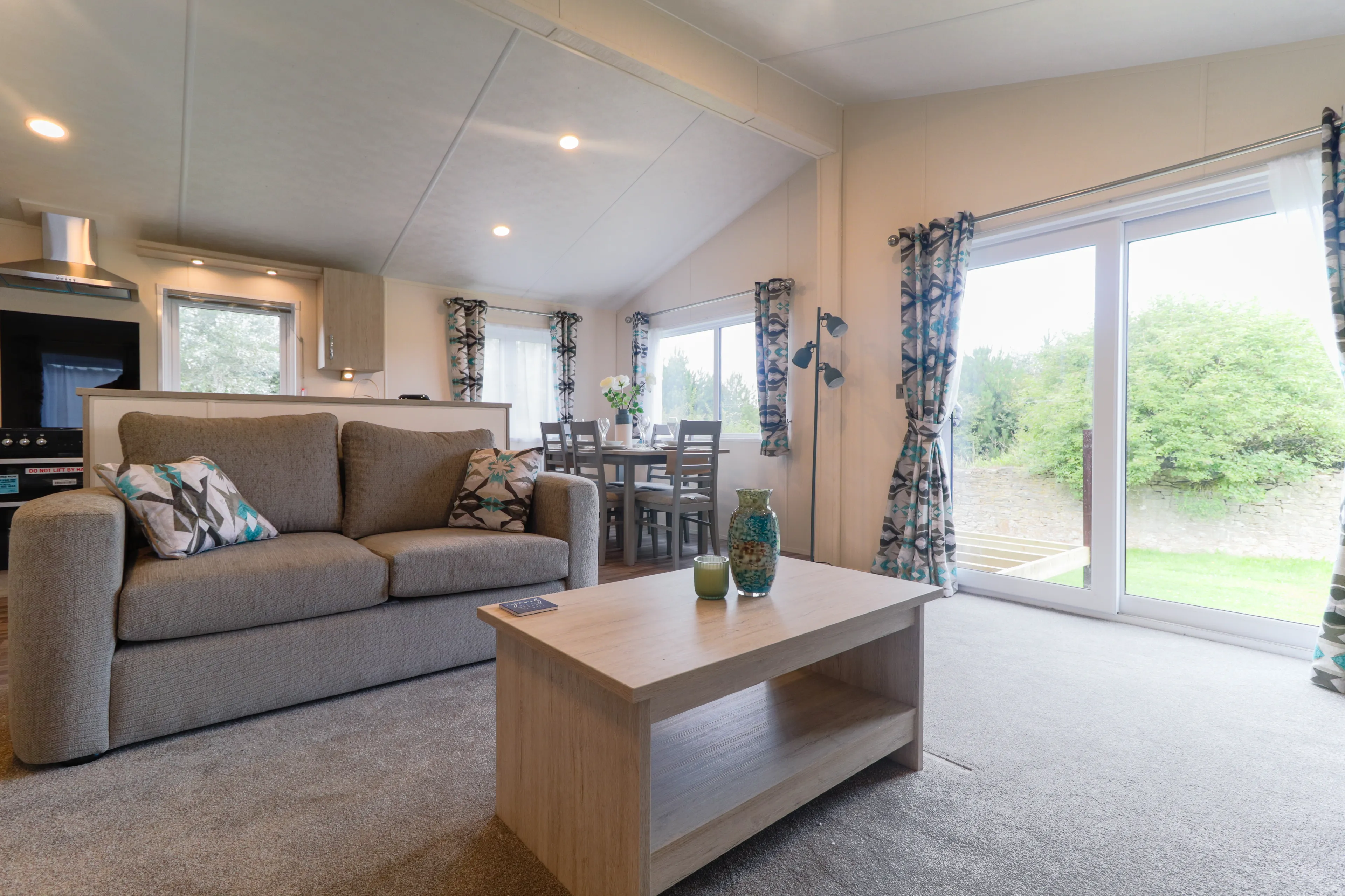 Modern open-plan living area with grey sofa, wooden coffee table, dining table and large sliding glass doors