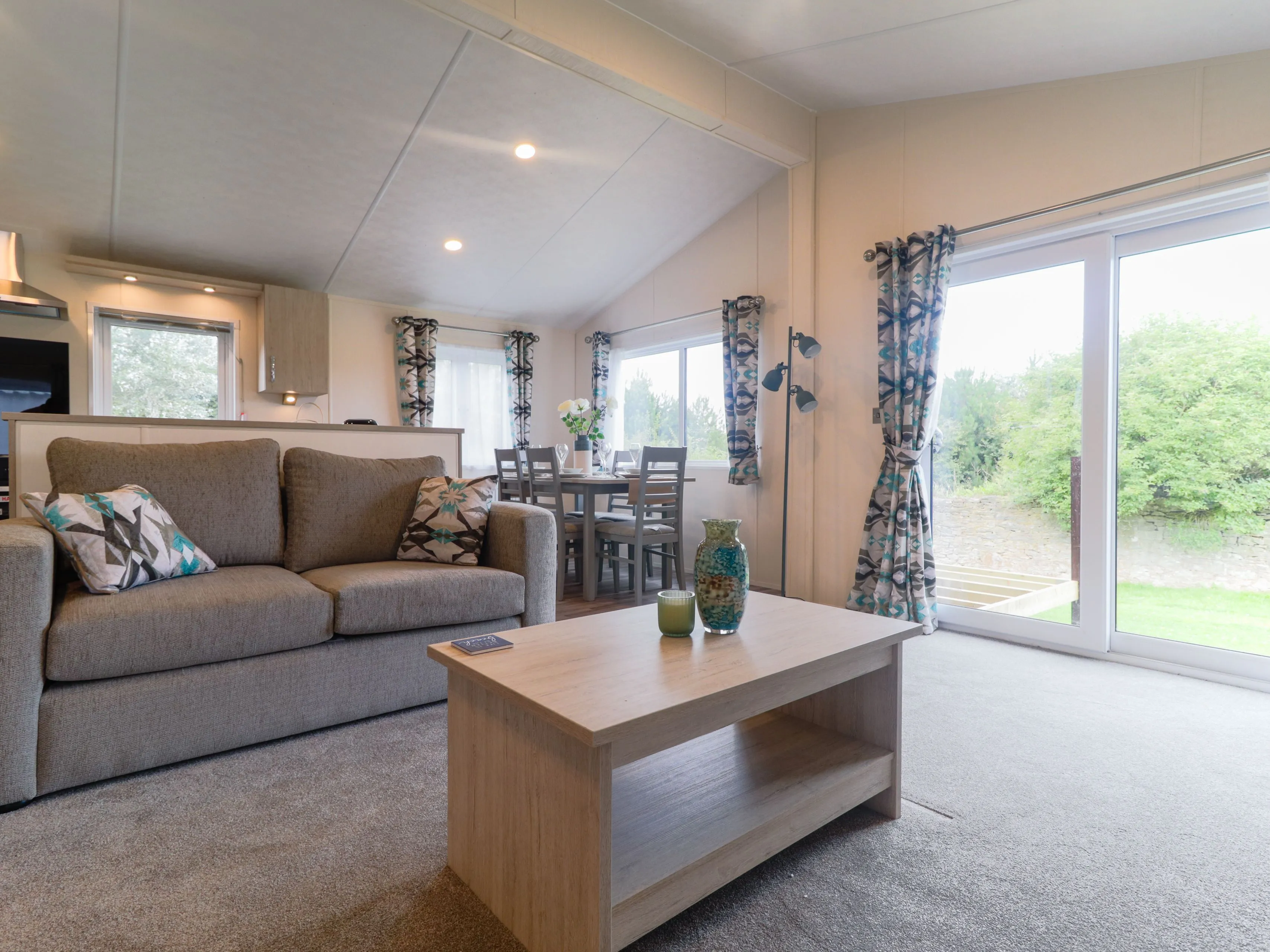 Modern open-plan living area with grey sofa, wooden coffee table, dining table and large sliding glass doors