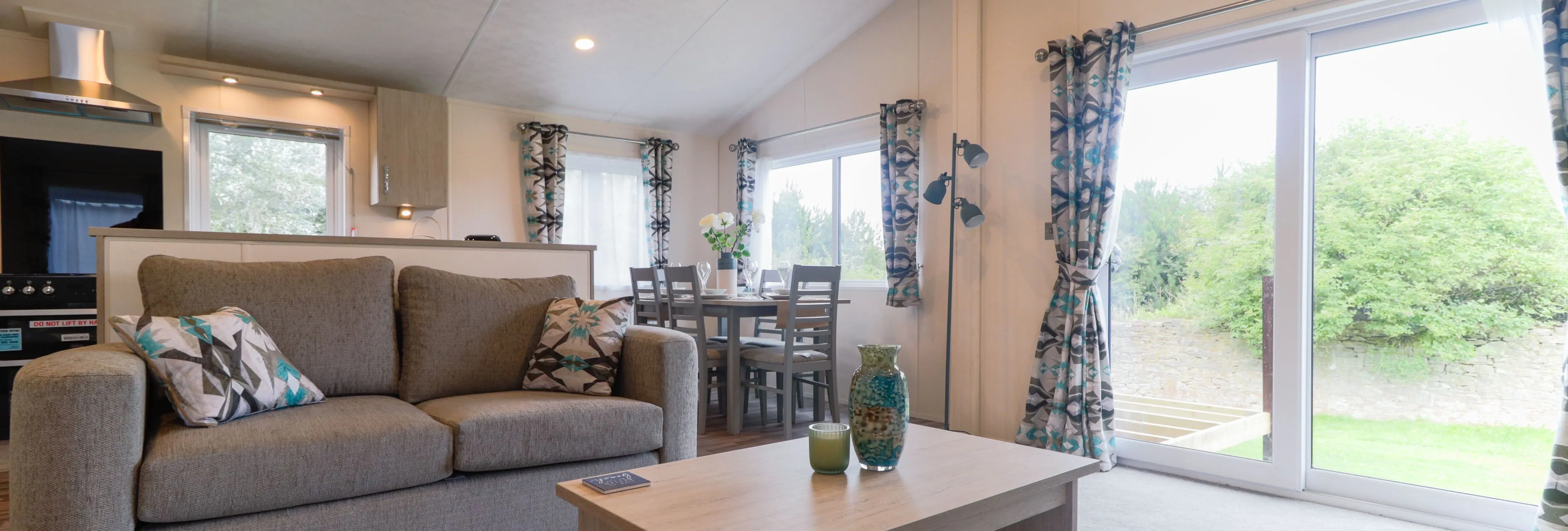 Modern open-plan living area with grey sofa, wooden coffee table, dining table and large sliding glass doors