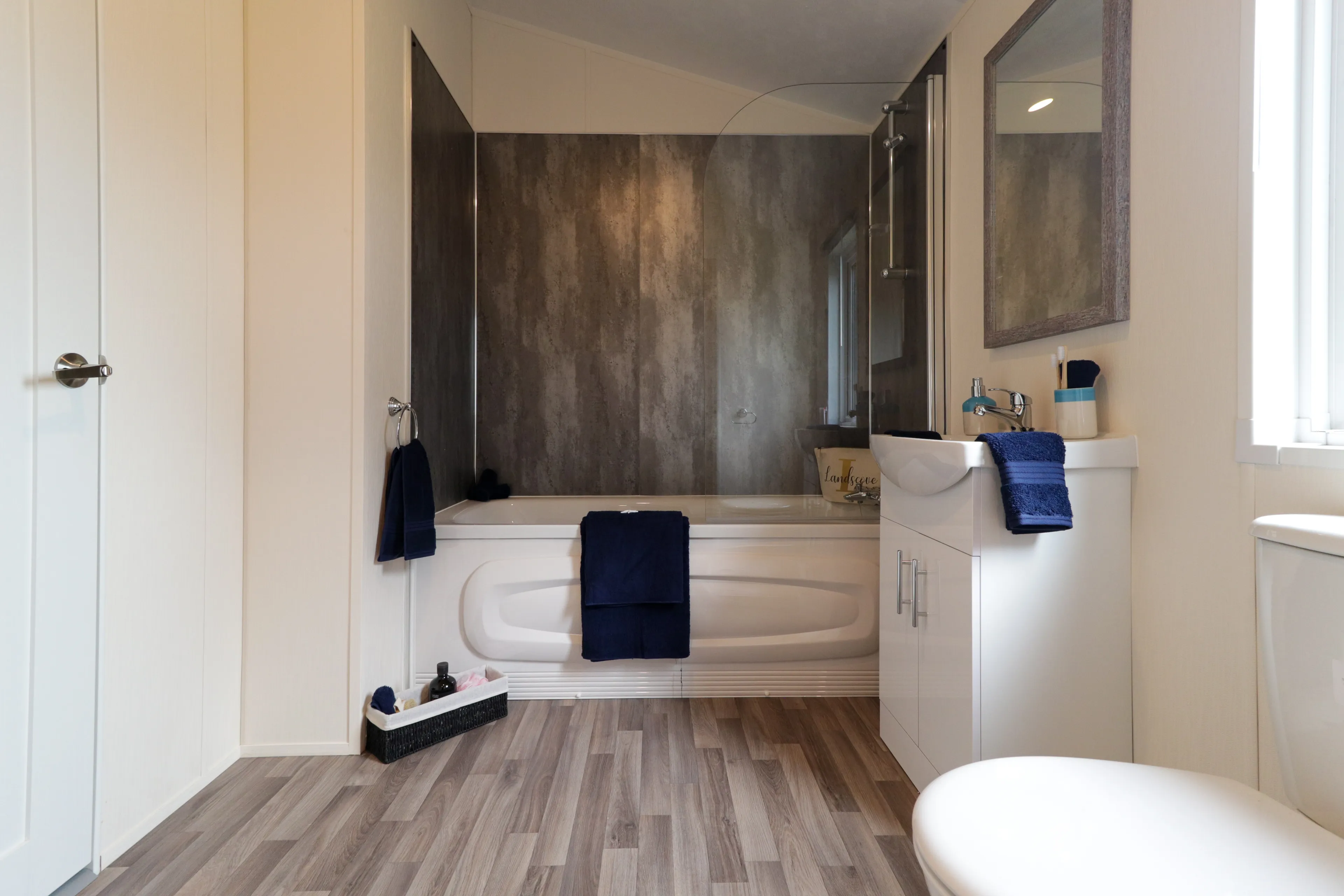 Modern bathroom with bathtub, glass shower screen, vanity unit and navy towels