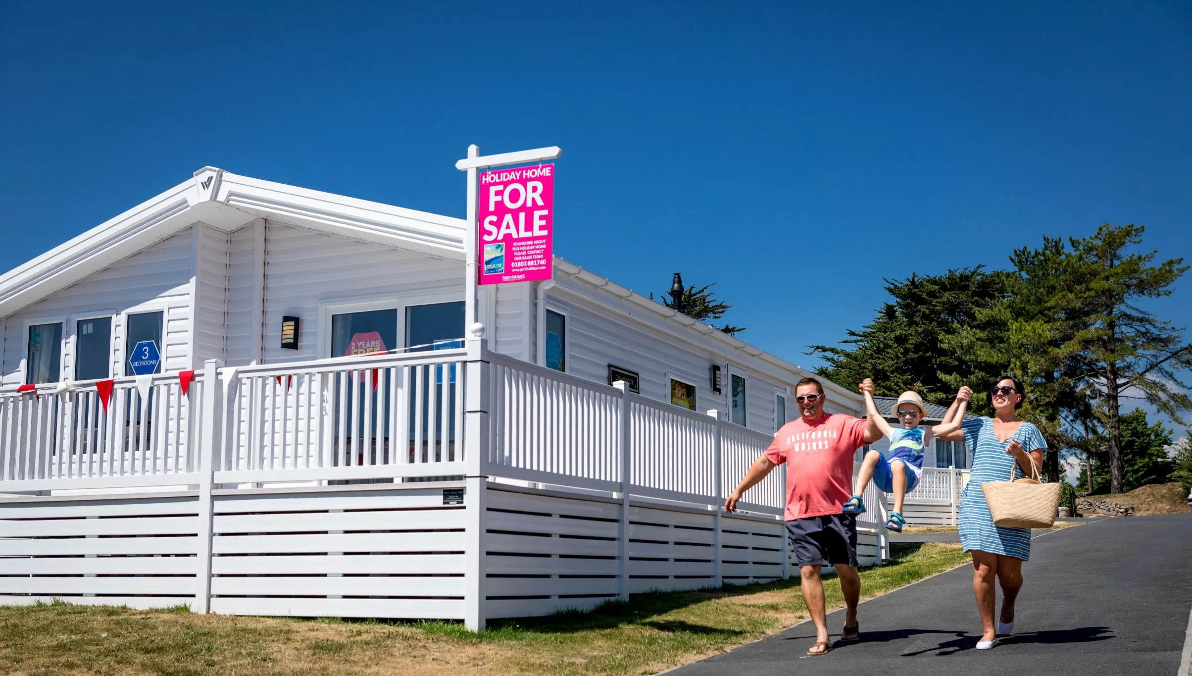 Family walking past a white holiday home with a 'For Sale' sign at Landscove Holiday Park