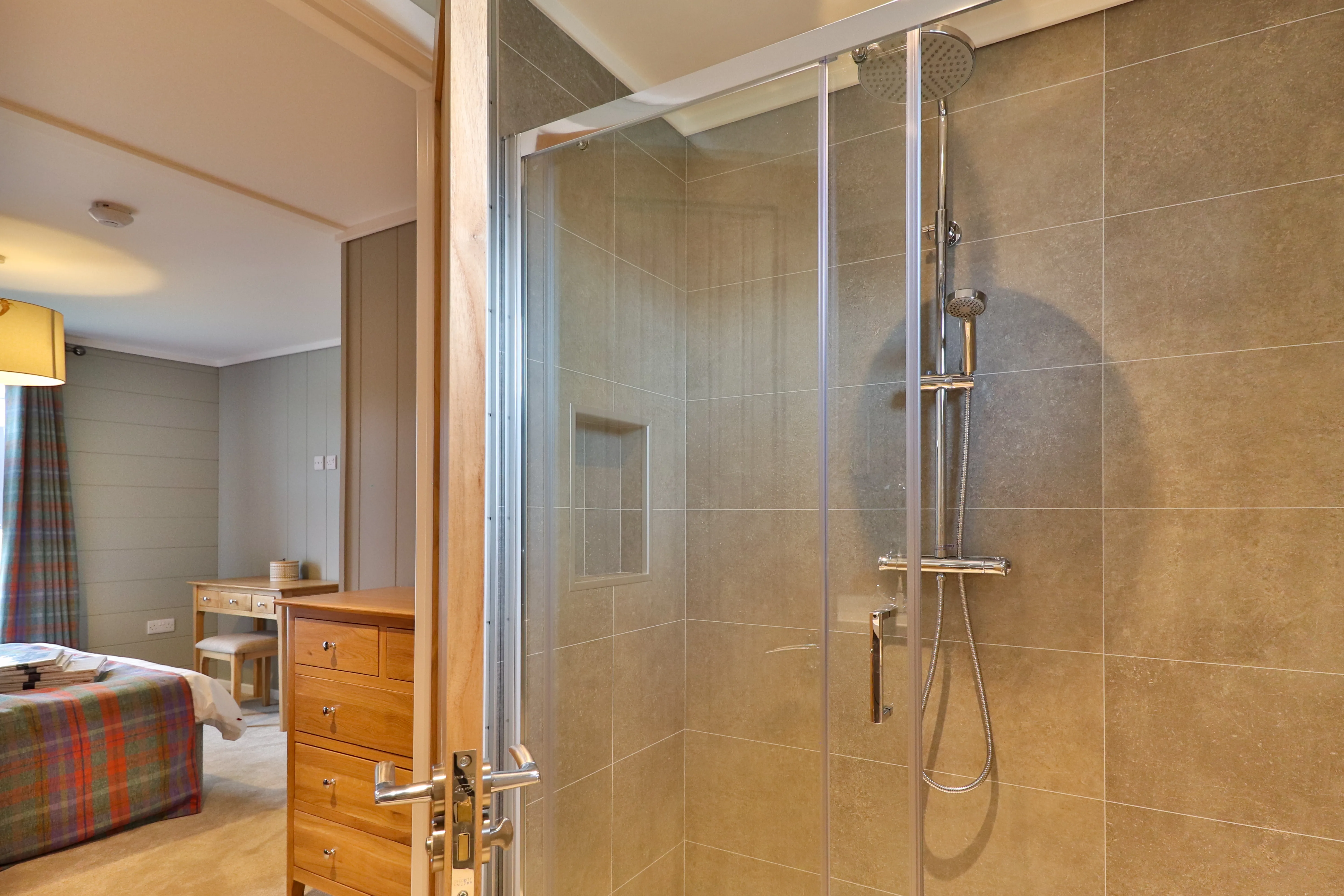 Glass-enclosed walk-in shower with rainfall showerhead and beige tiled walls beside a cosy bedroom