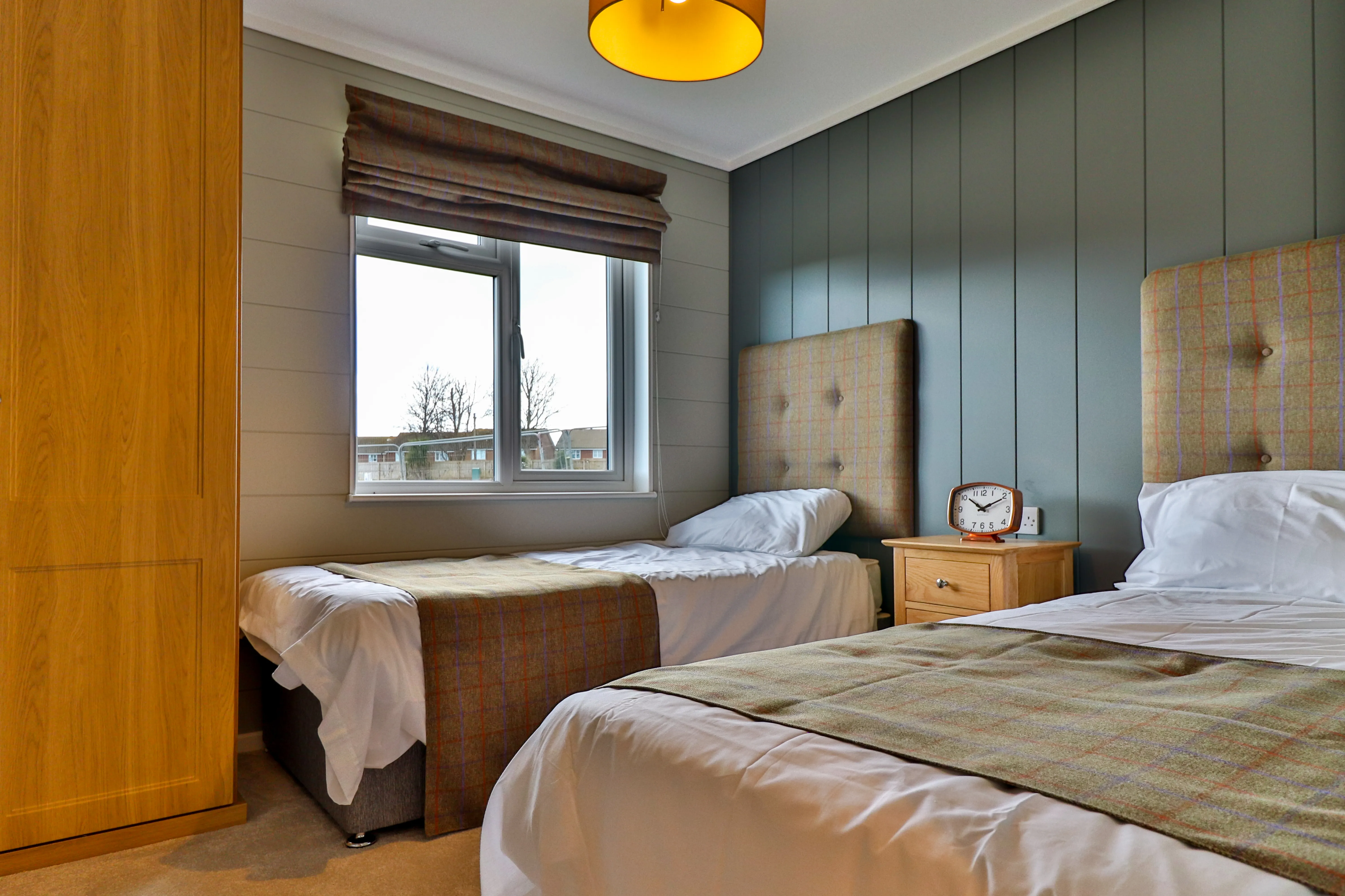 Twin bedroom with two single beds, grey panelling, and a window with a roman blind