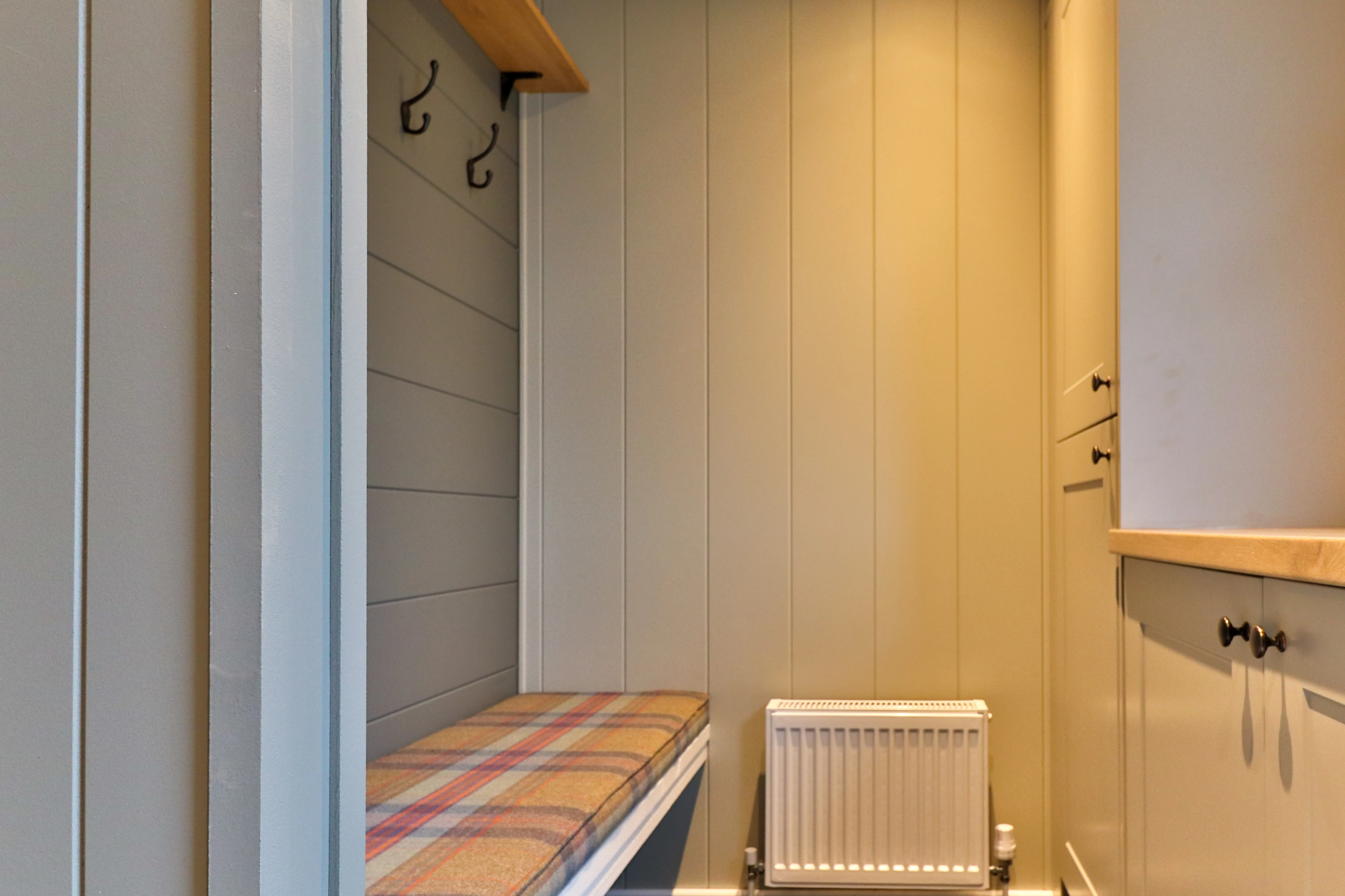 Cosy hallway alcove with a tartan bench seat, coat hooks and a radiator