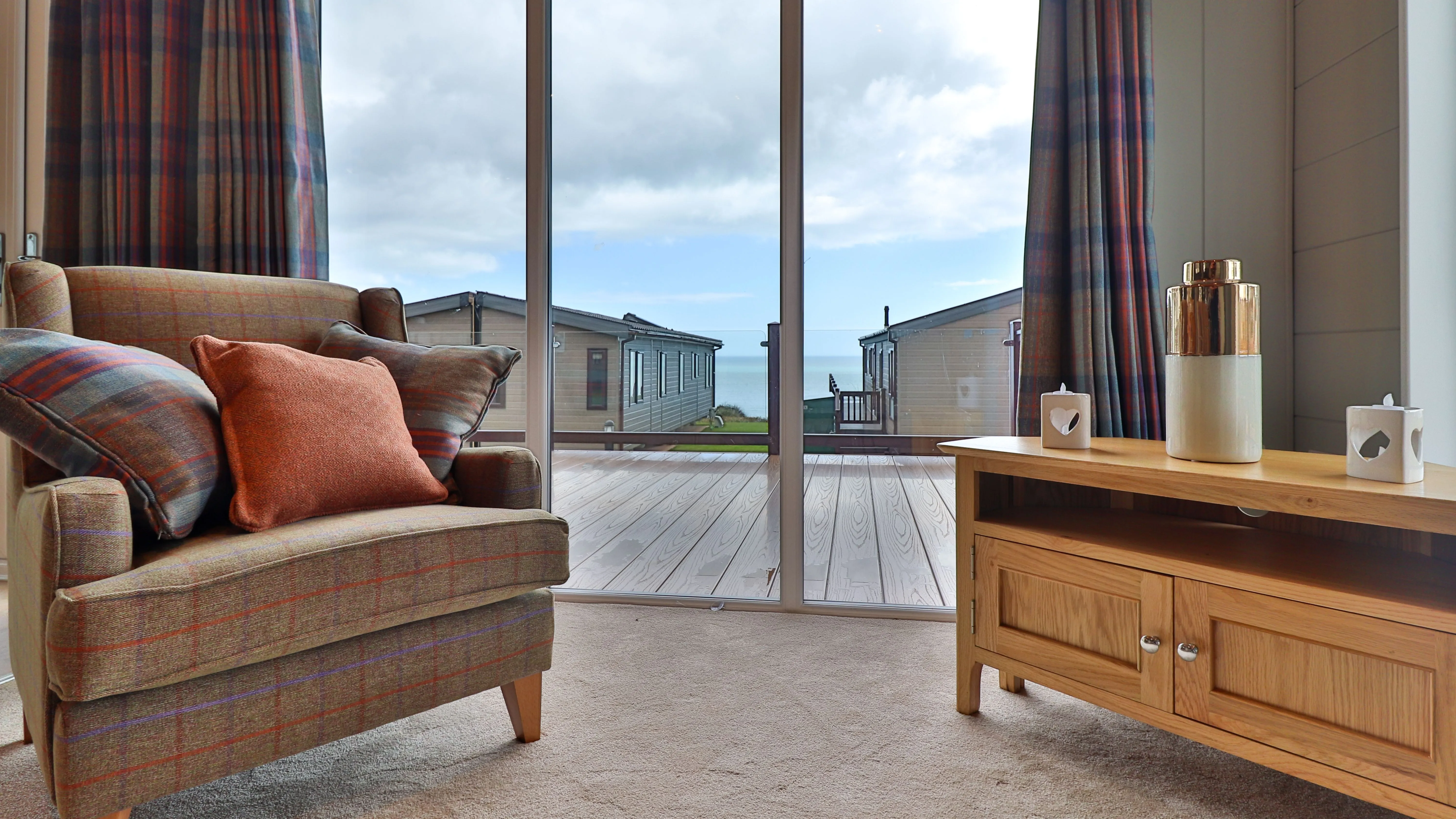 Cosy living room with armchair and wooden TV unit facing large glass doors to a seaside deck