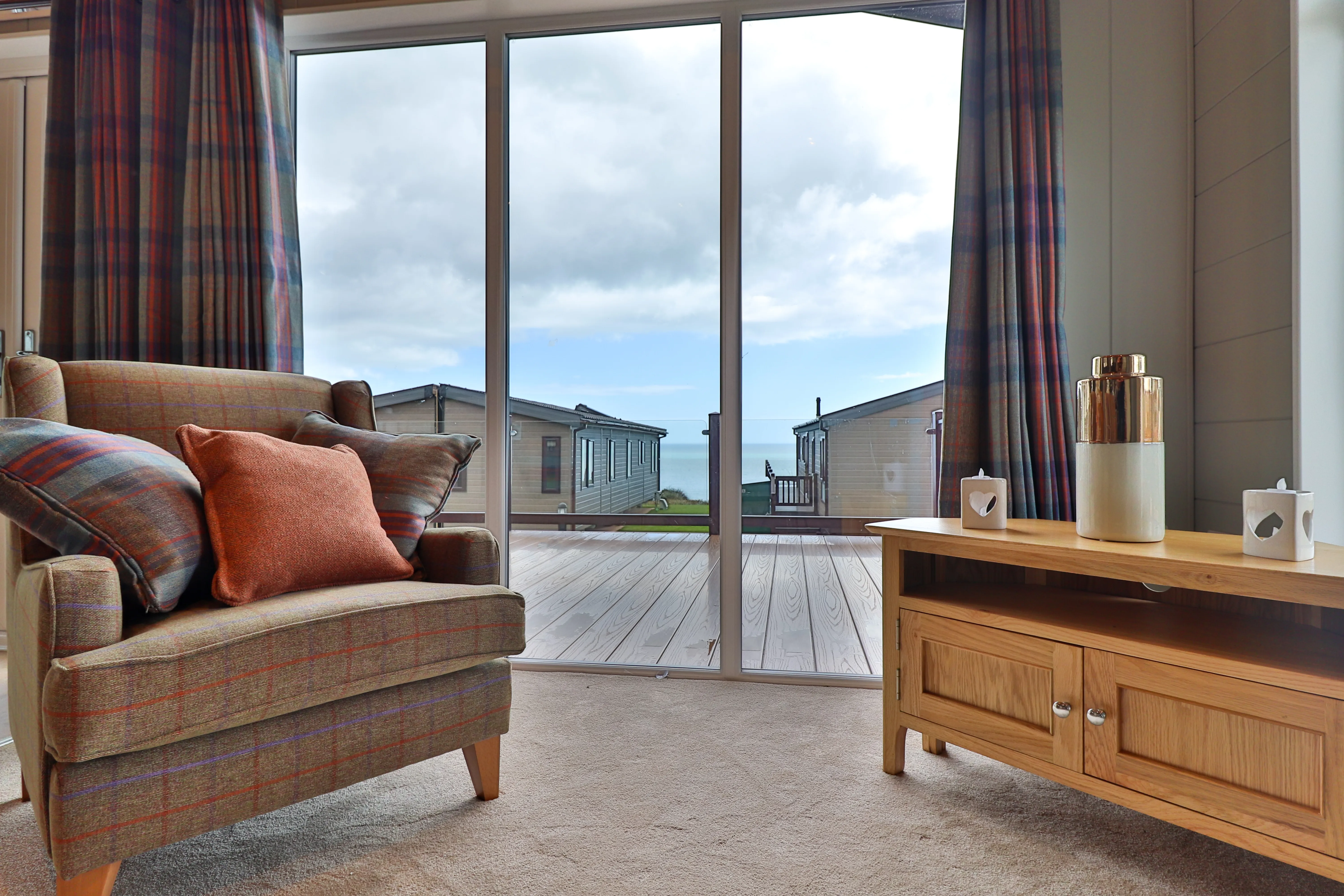 Cosy living room with armchair and wooden TV unit facing large glass doors to a seaside deck