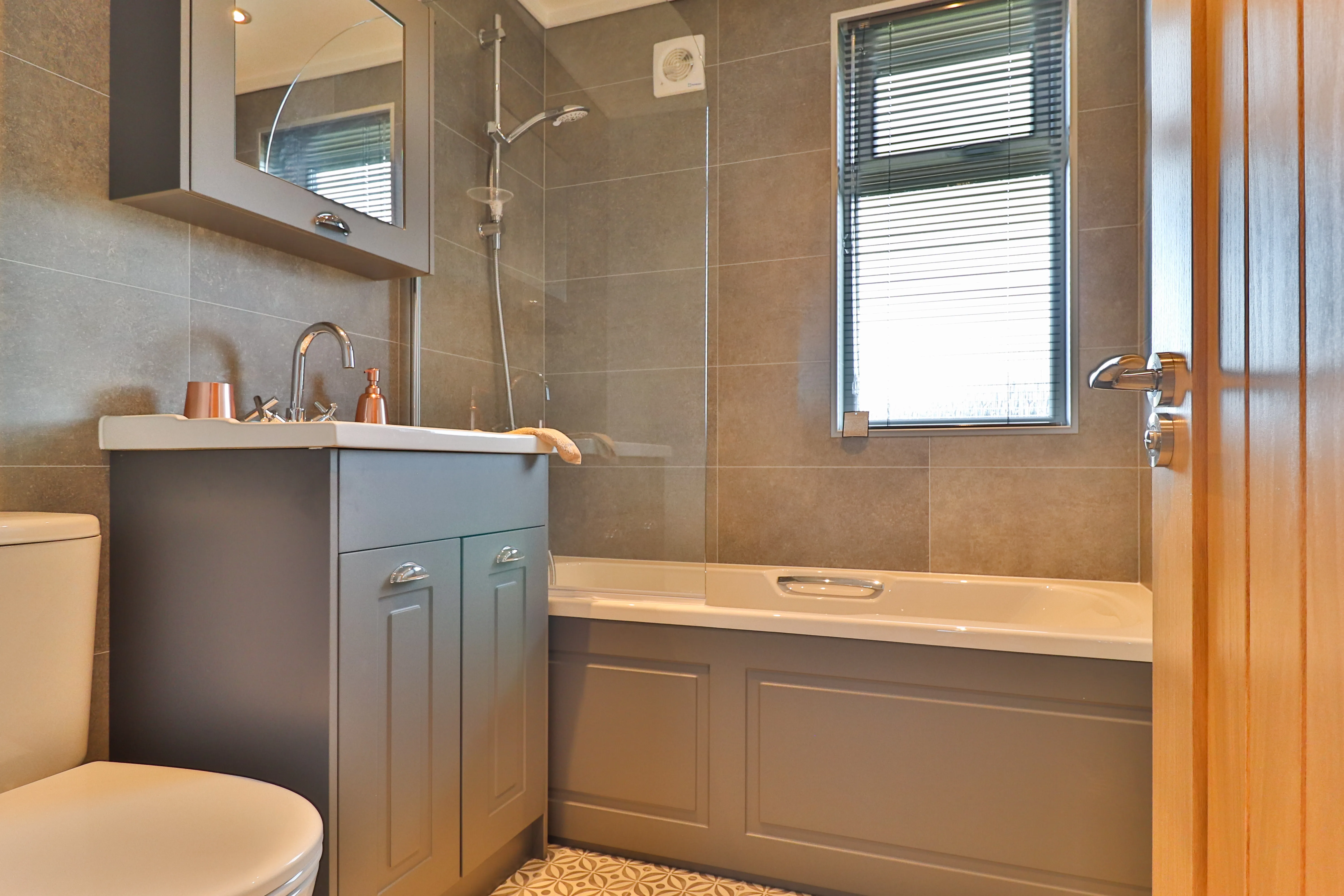 Modern bathroom with grey vanity, bathtub with shower screen, and window blinds
