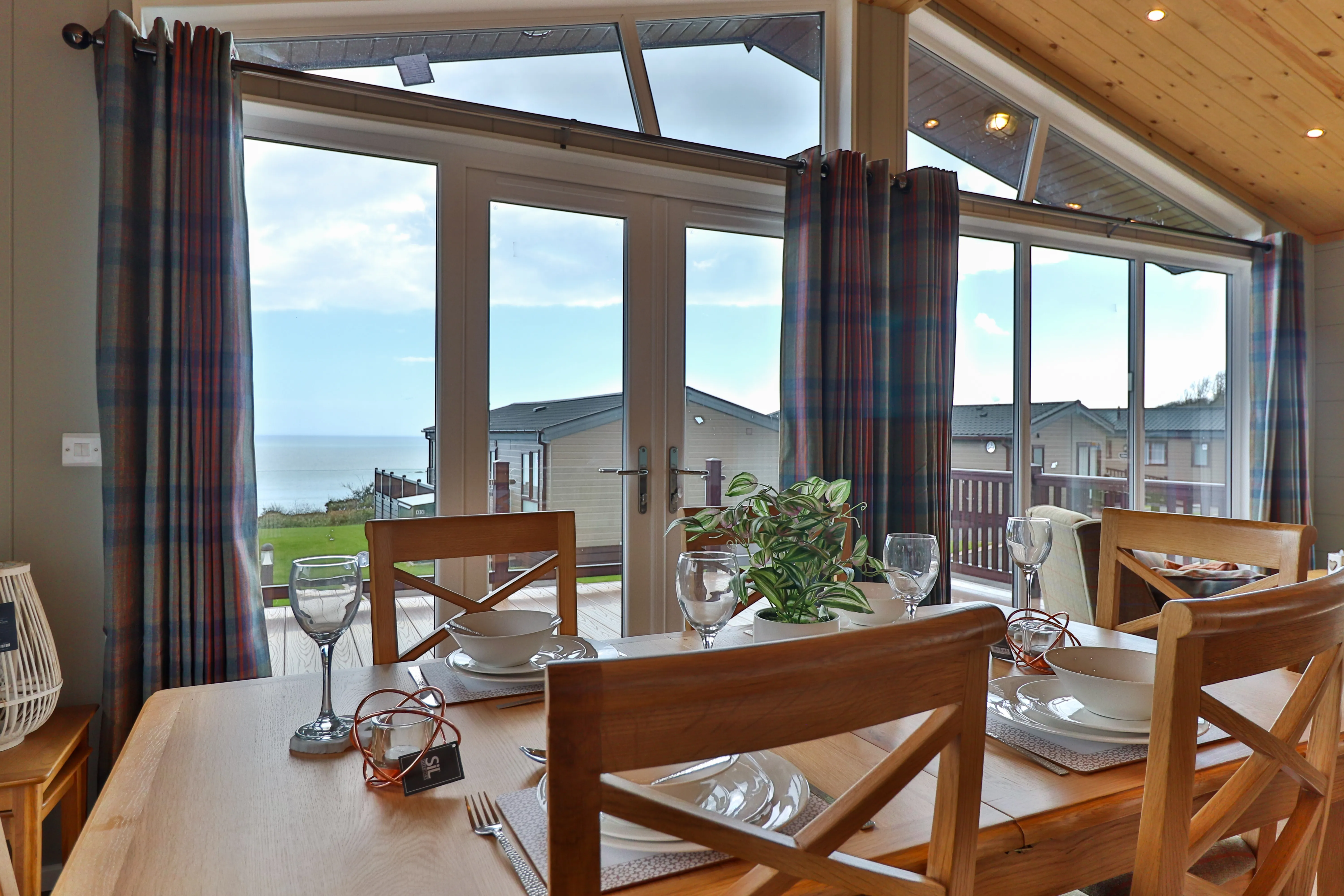 Dining table set by large windows with sea view and coastal cabins outside