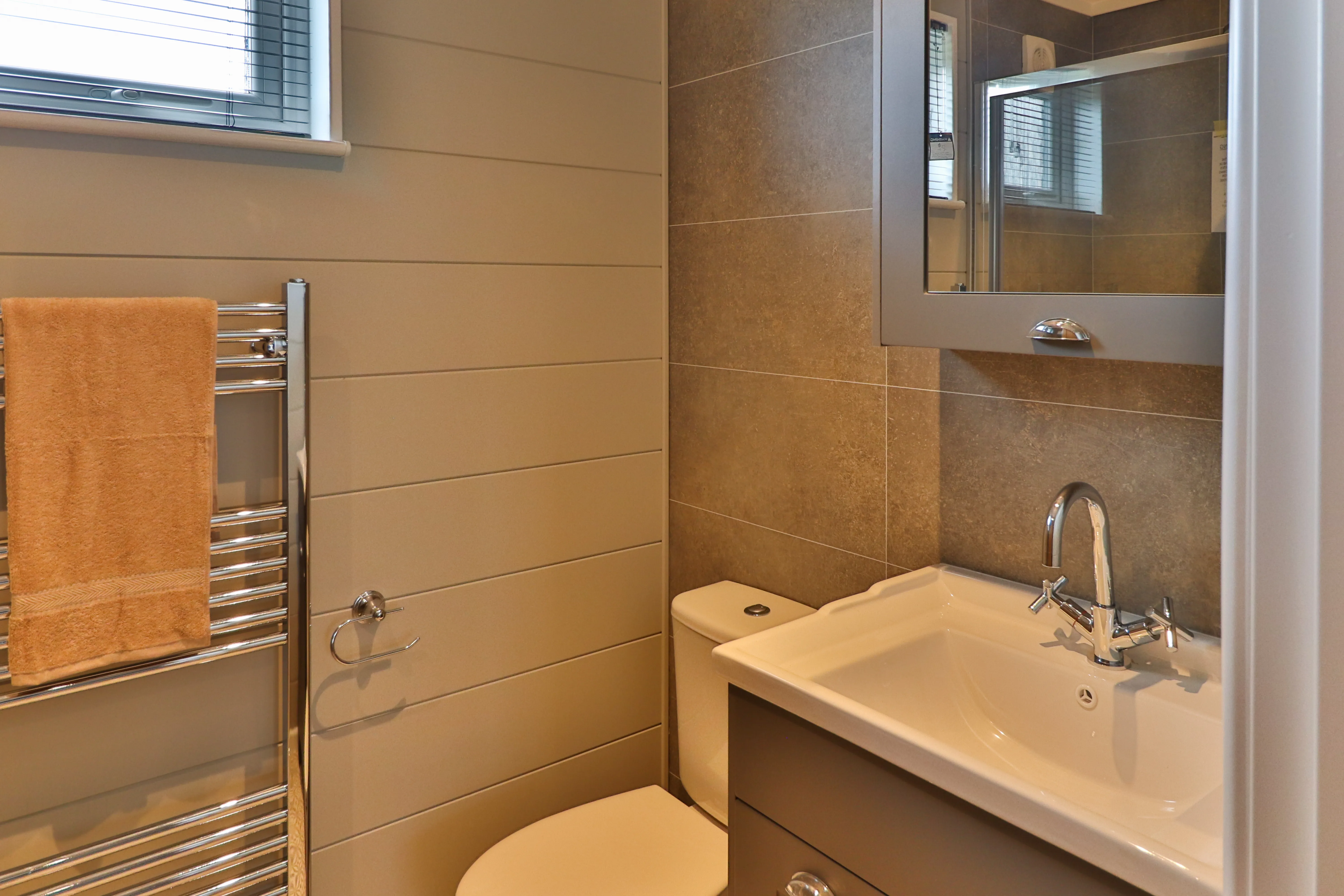 Modern bathroom with grey tiles, vanity sink, mirror, toilet and towel radiator