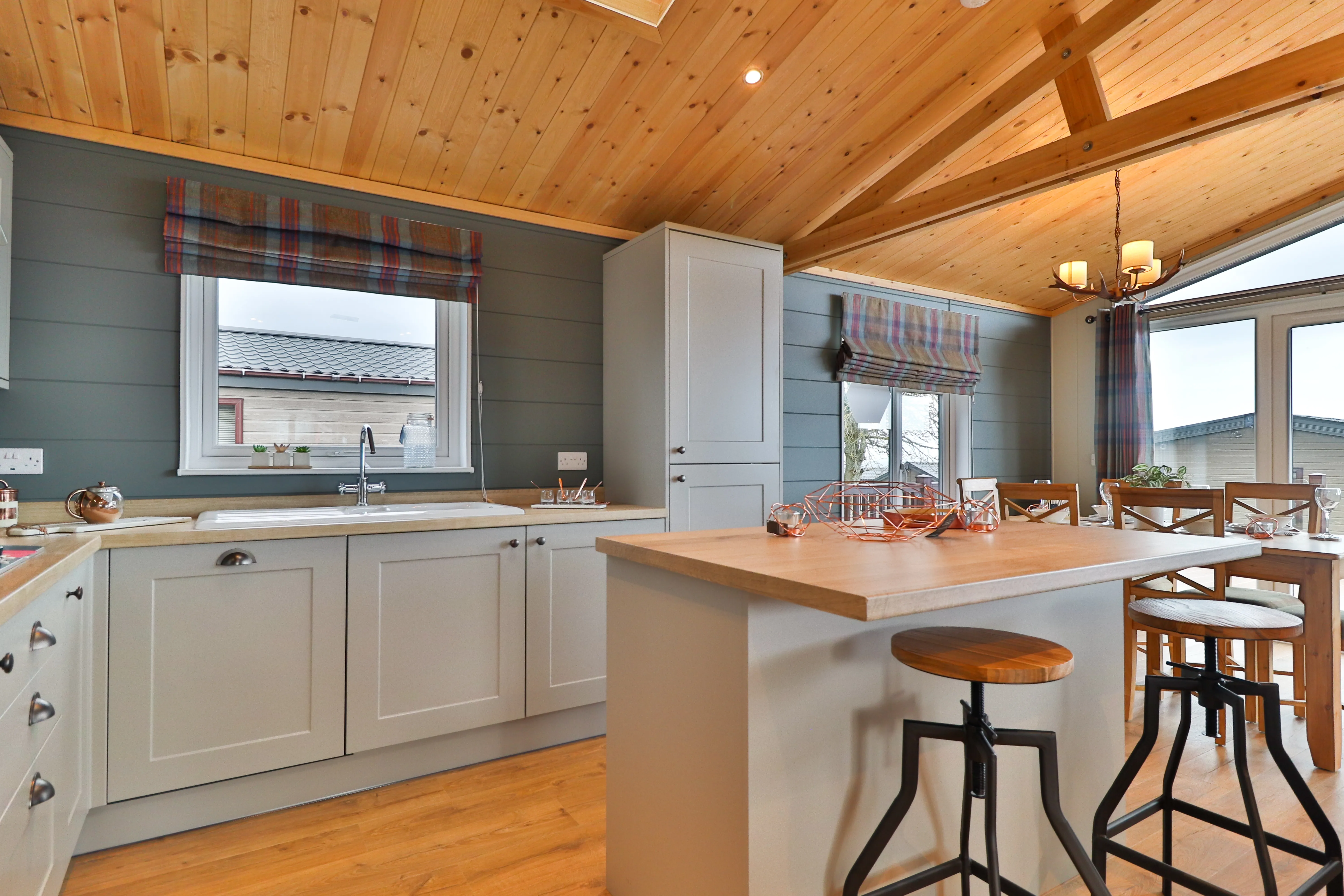 Modern kitchen and dining area with grey cabinets, wooden ceiling and a breakfast island