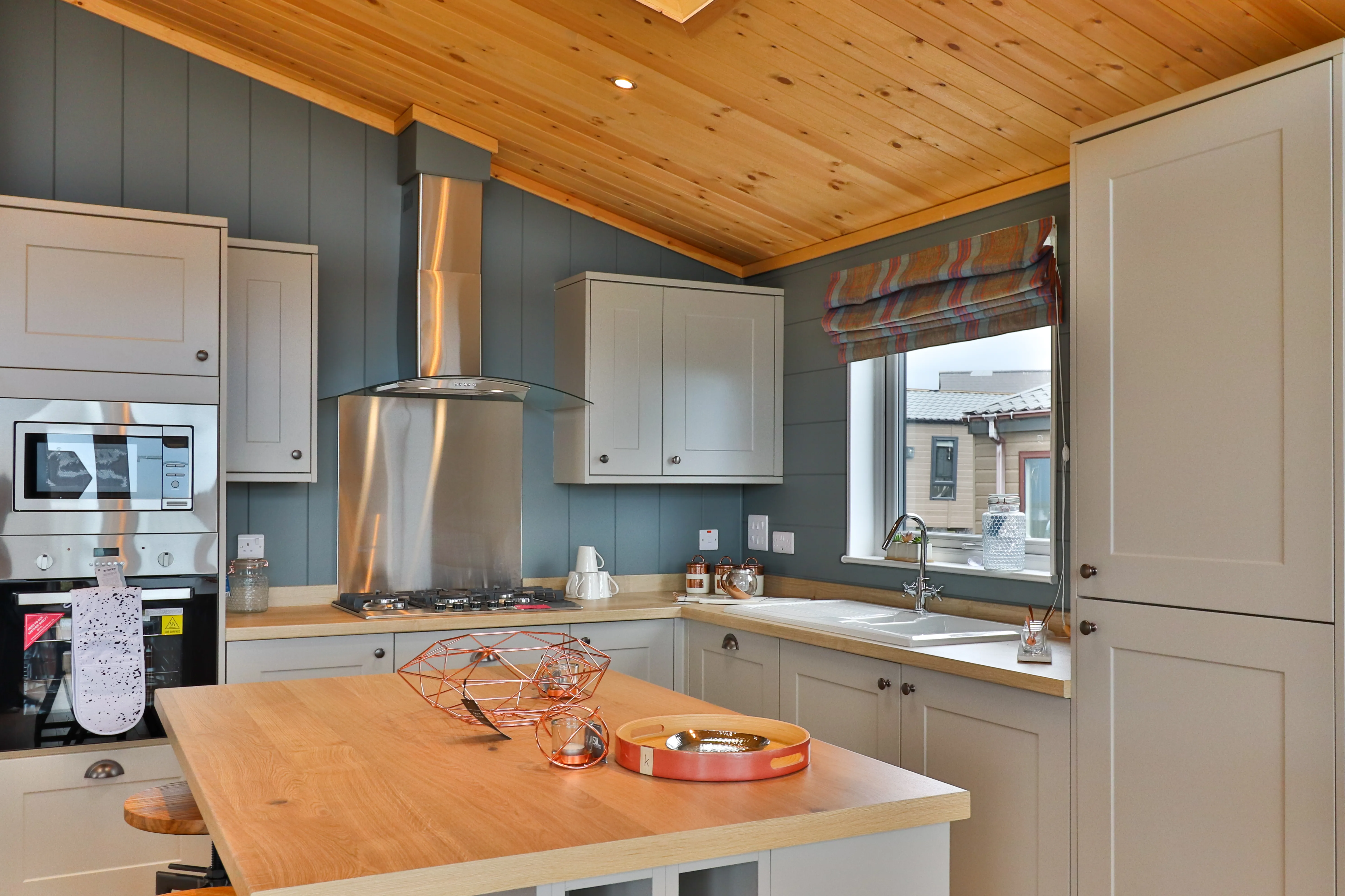 Modern kitchen with wooden ceiling, grey cabinets, stainless steel cooker hood and island worktop