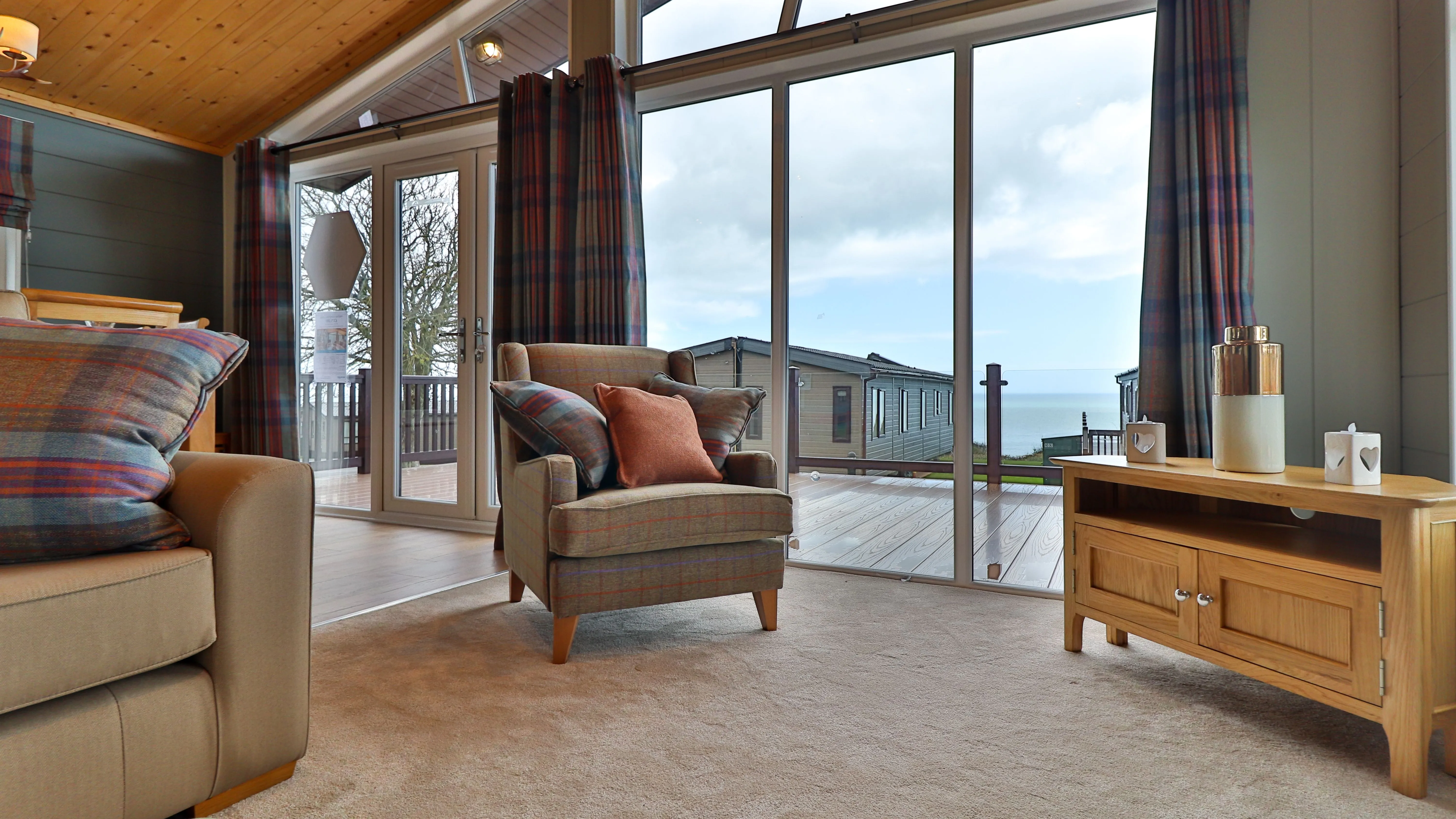 Cosy living room with armchair, sofa and large glass doors overlooking a deck and sea view