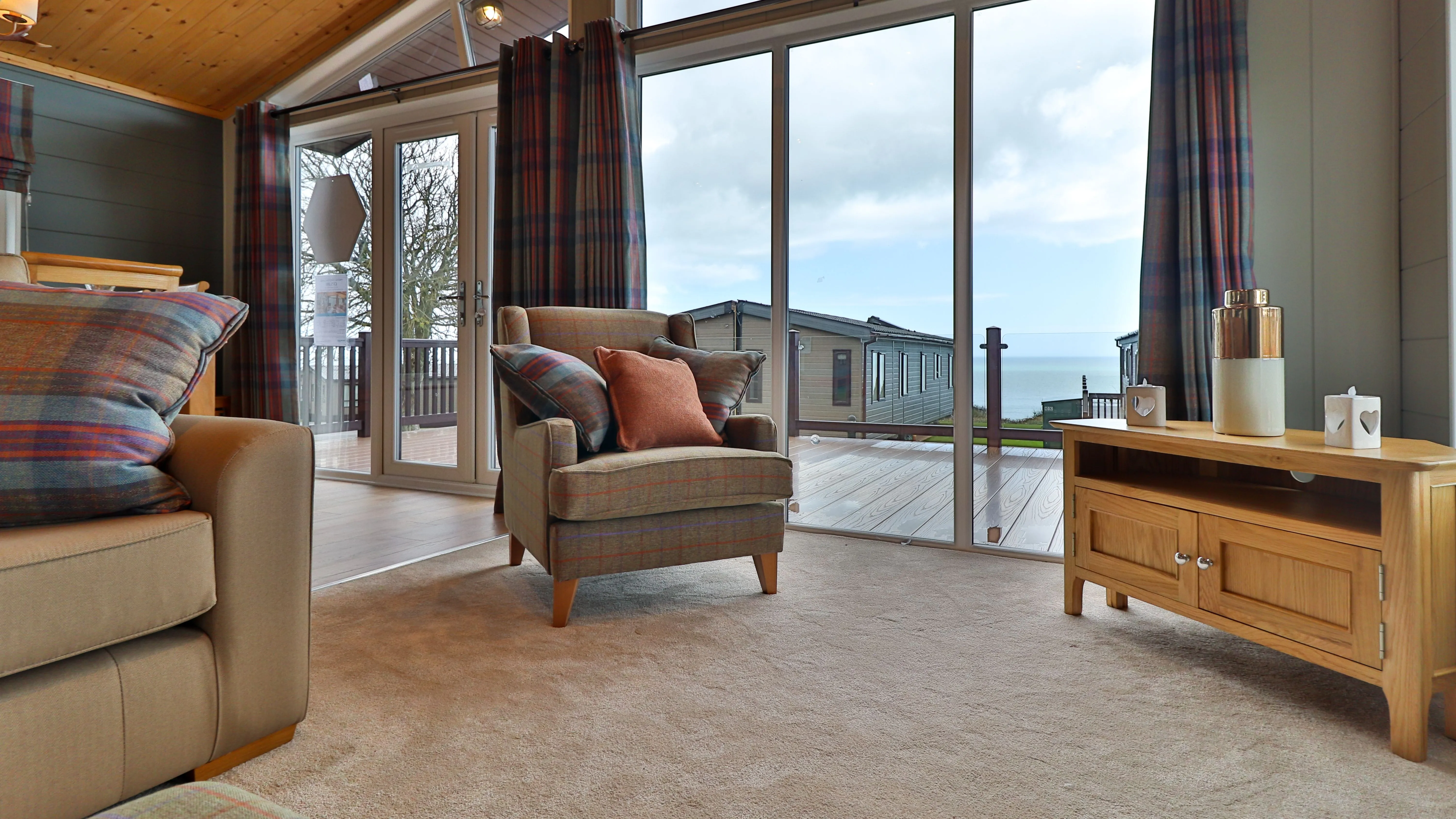 Cosy living room with armchair, sofa and large glass doors overlooking a deck and sea view