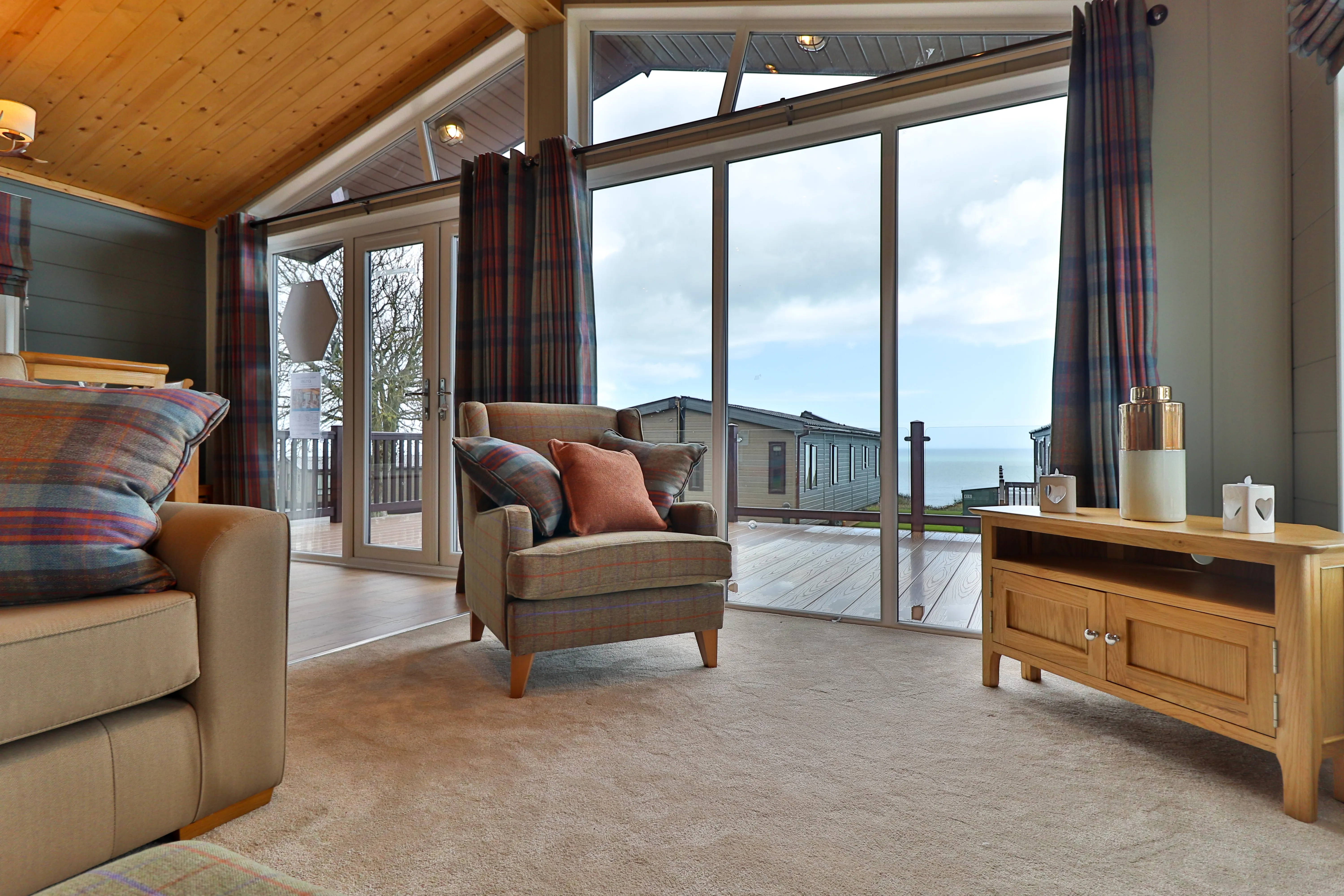 Cosy living room with armchair, sofa and large glass doors overlooking a deck and sea view